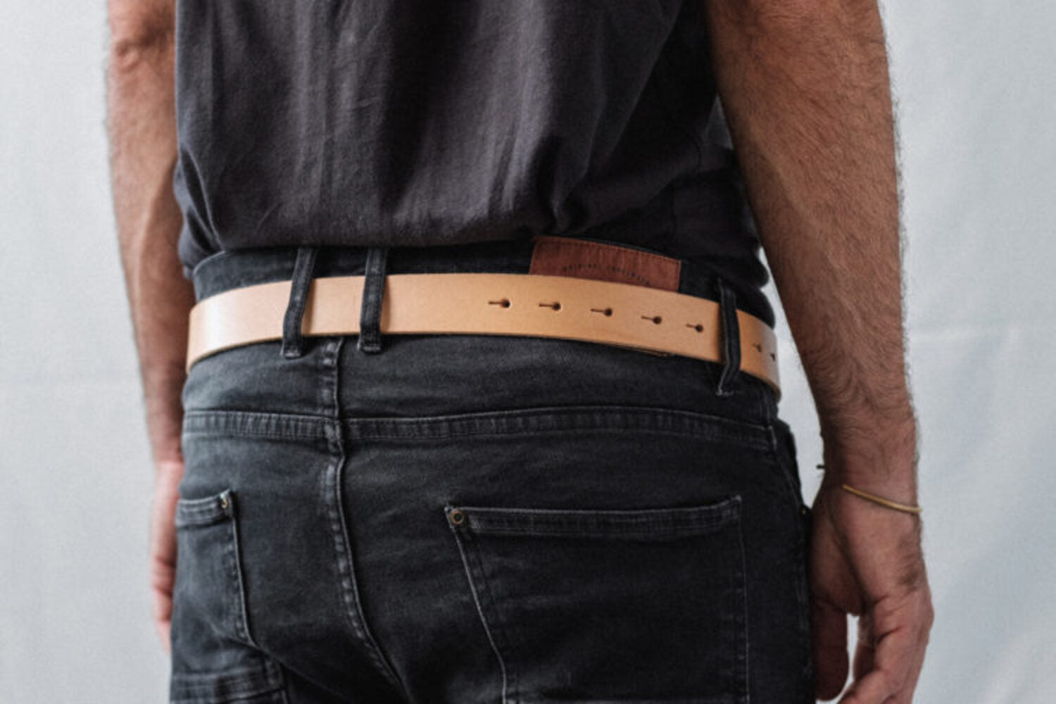 Back view of a man wearing a tan leather belt with black jeans, emphasizing the clean and functional design.