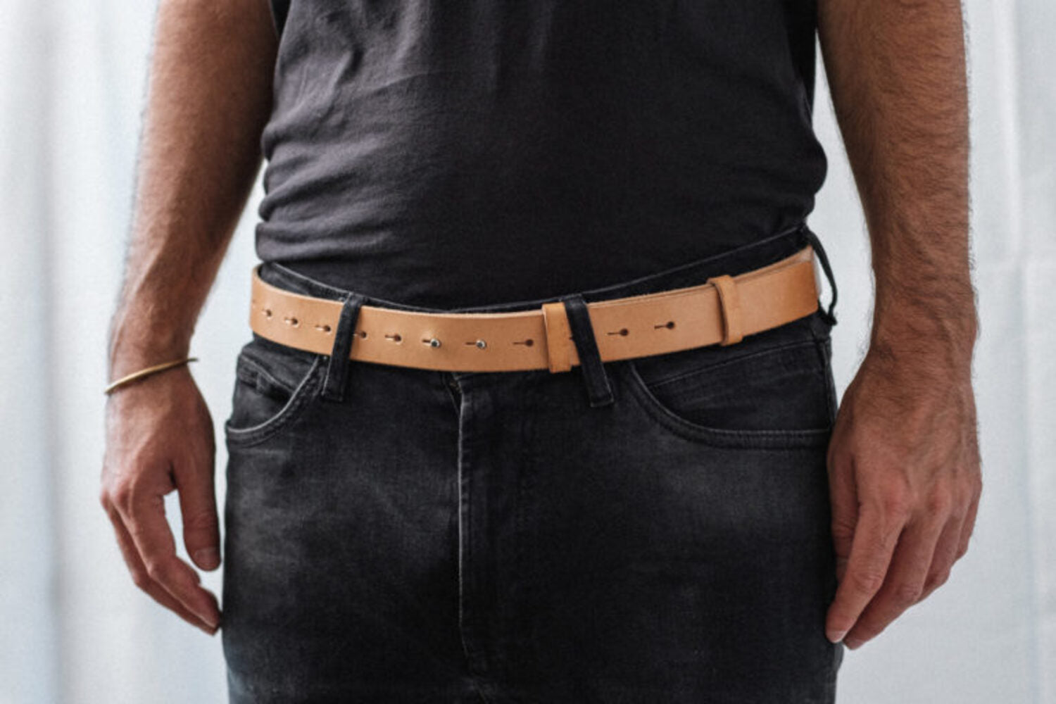 Frontal close-up of Lobo Apparel natural leather belt fastened at the waist, with visible pin closure over black trousers.