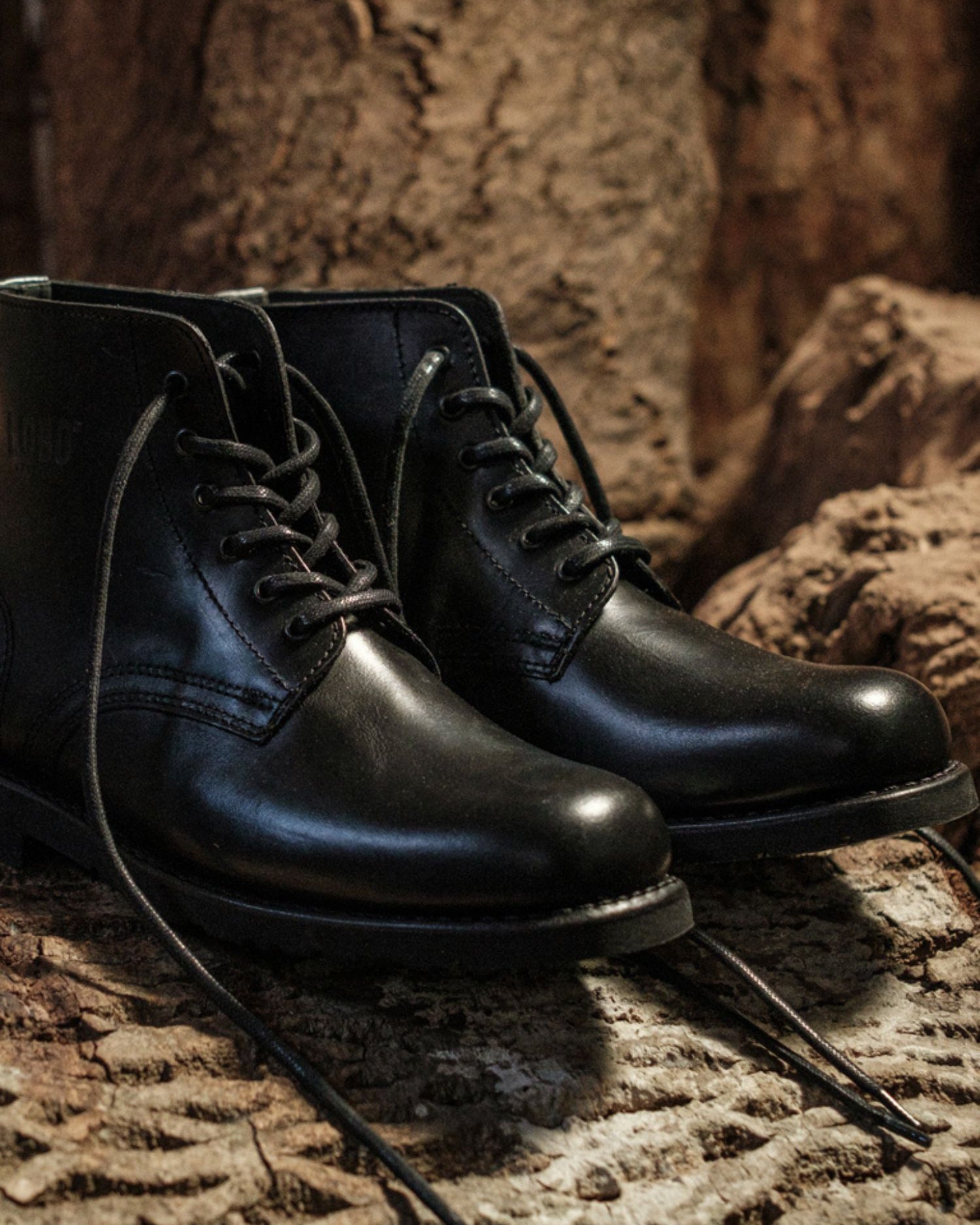 Pair of Lobo All Black leather boots with black cotton laces, Goodyear Welt construction, on a rustic background.