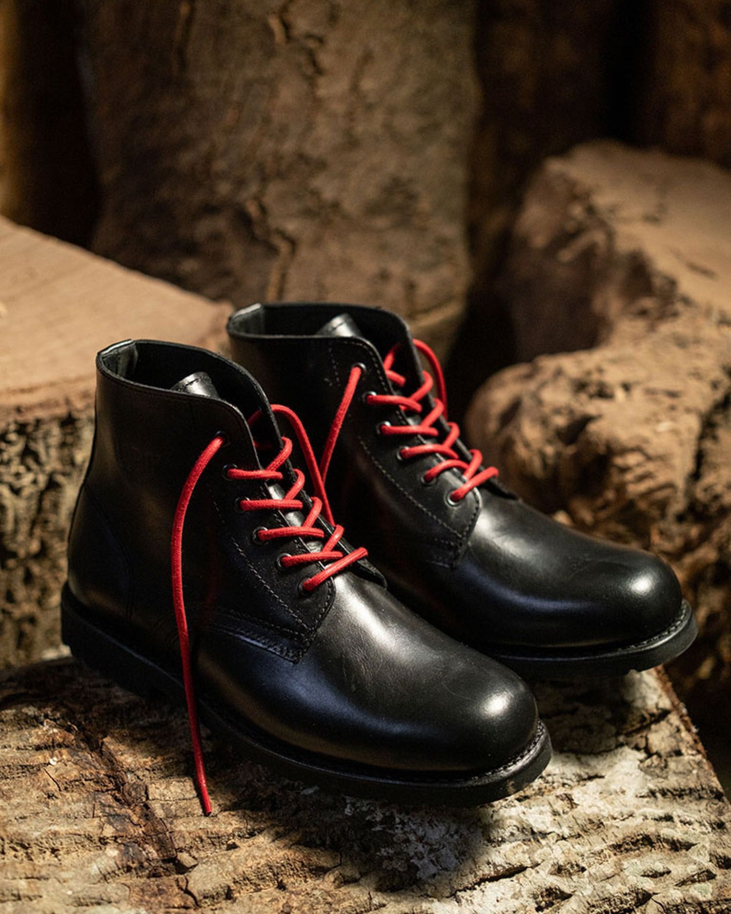 Lobo All Black leather boots with red cotton laces on a textured wood surface