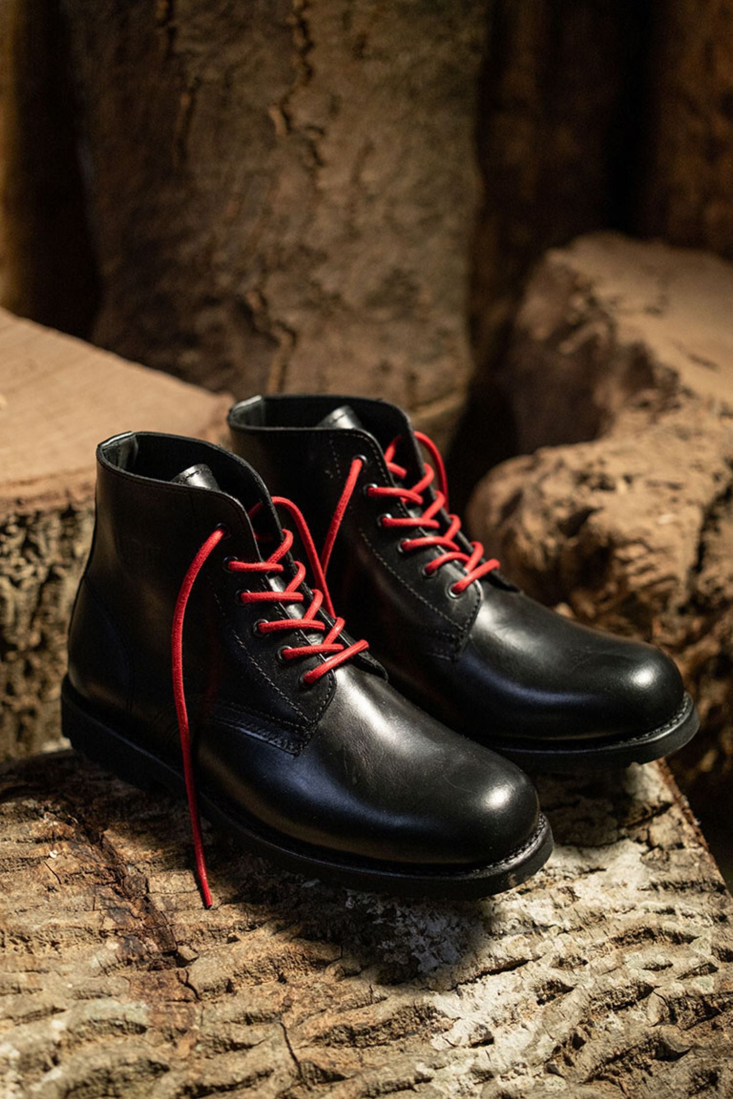 Lobo All Black leather boots with red cotton laces on a textured wood surface
