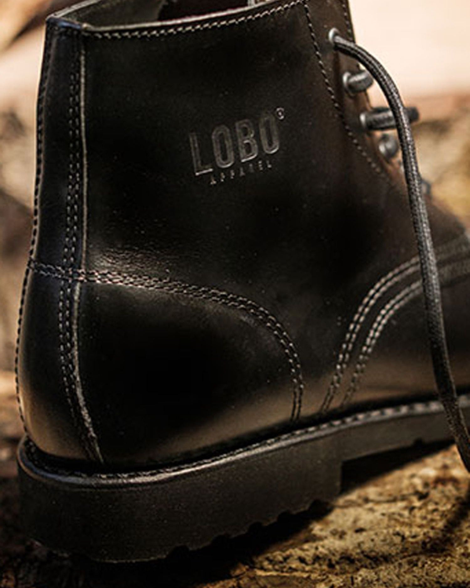 Close-up of the Lobo Apparel logo stamped on the black leather of All Black boots, showing stitching.