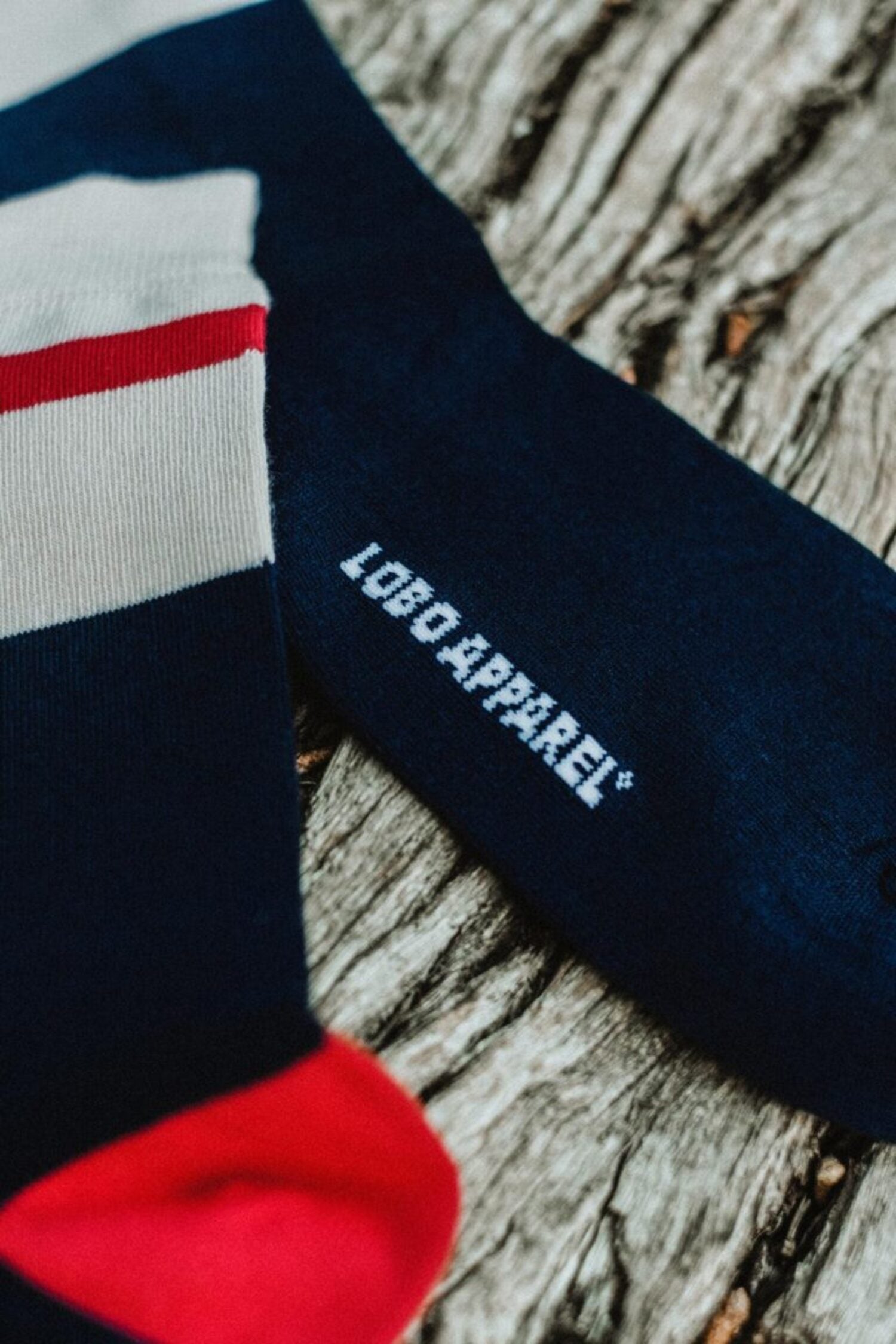 Close-up detail of the "LOBO APPAREL" logo embroidered in white on the side of a premium dark blue knit sock.