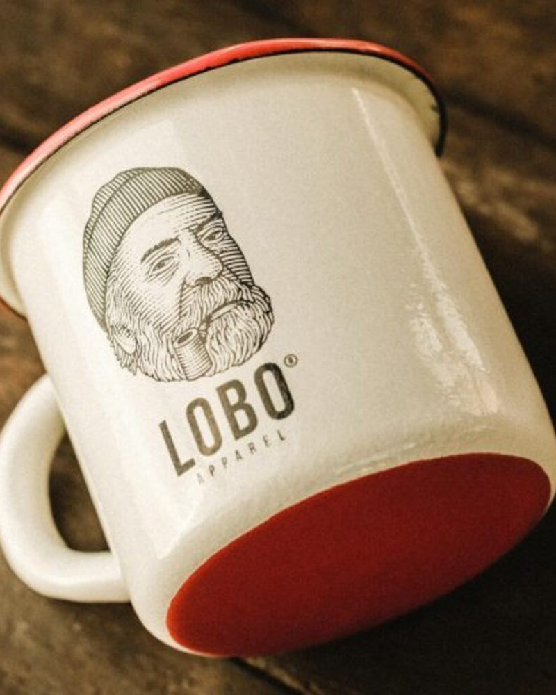 LOBO enamel mug tilted on a wooden table, revealing the vibrant red base and the sturdiness of the material.