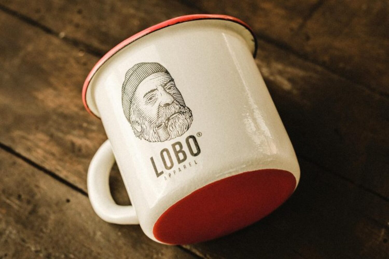 LOBO enamel mug tilted on a wooden table, revealing the vibrant red base and the sturdiness of the material.