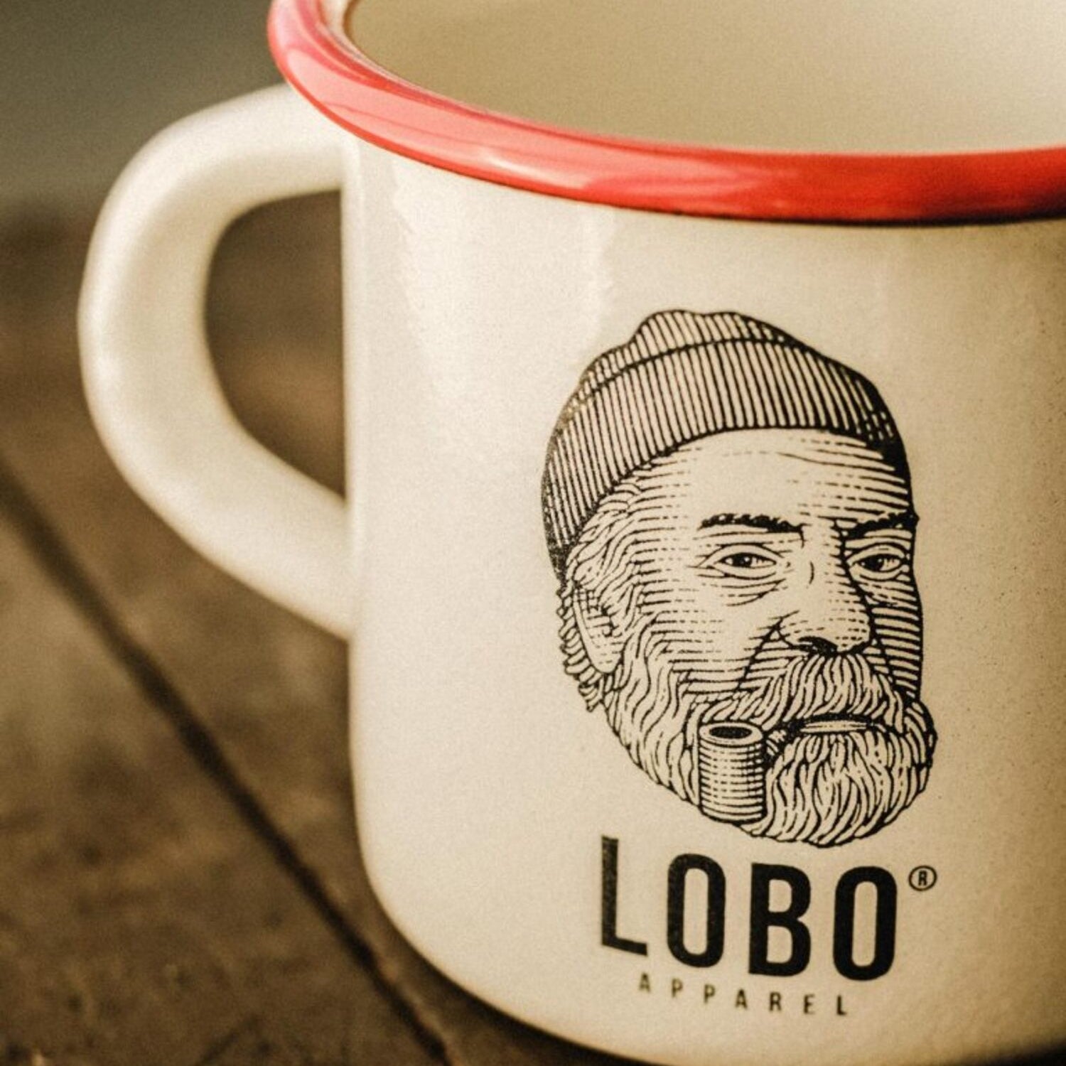 Close-up detail of the print on the LOBO enamel mug, highlighting the logo of the man with a beanie and pipe and the glossy finish.