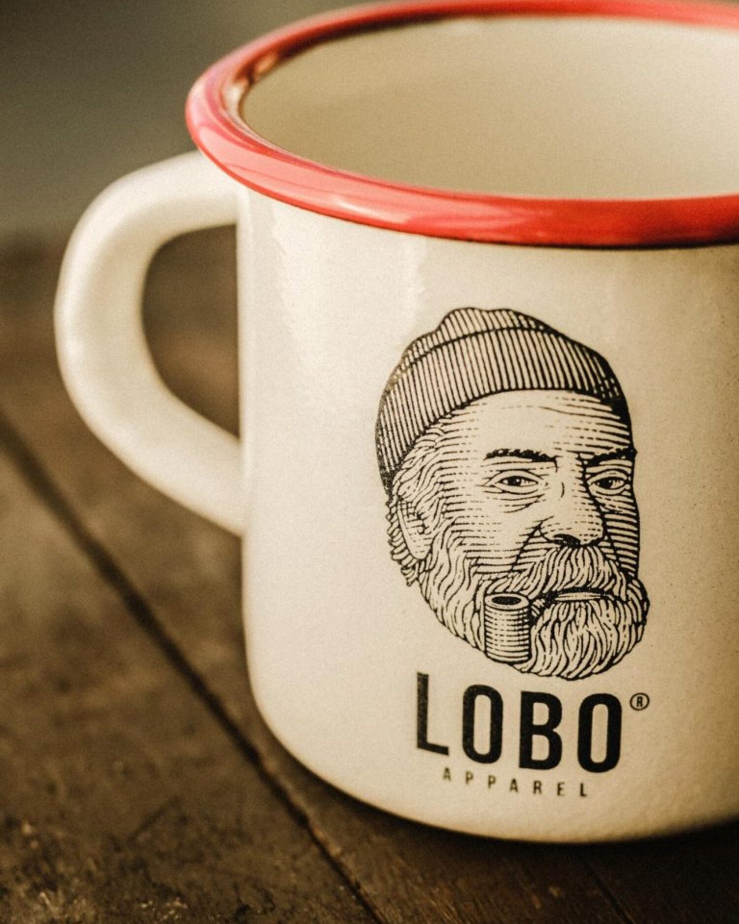 Close-up detail of the print on the LOBO enamel mug, highlighting the logo of the man with a beanie and pipe and the glossy finish.