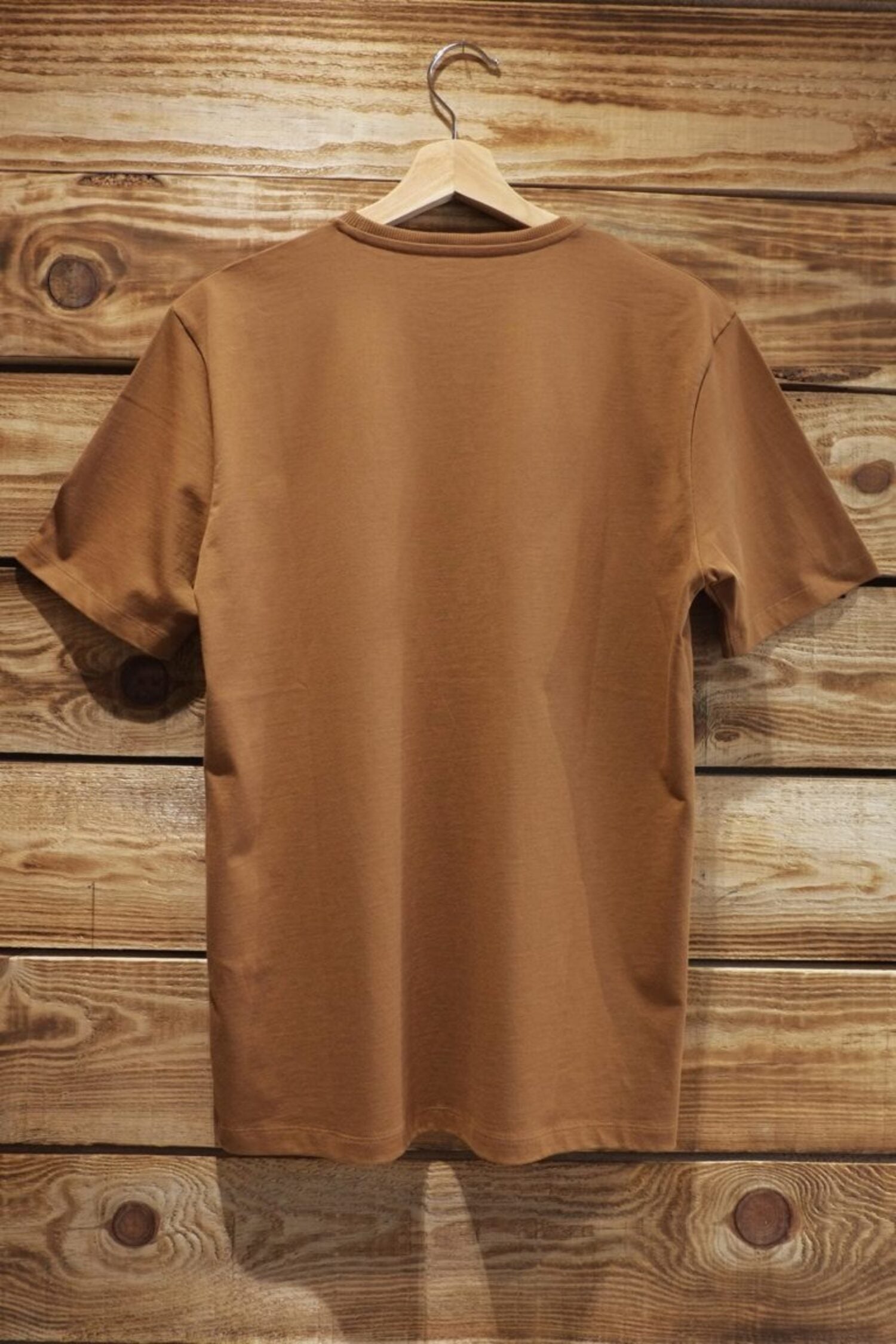 Back view of the Lobo "Natureza" t-shirt in brown, hanging on a wooden hanger against a wooden background.