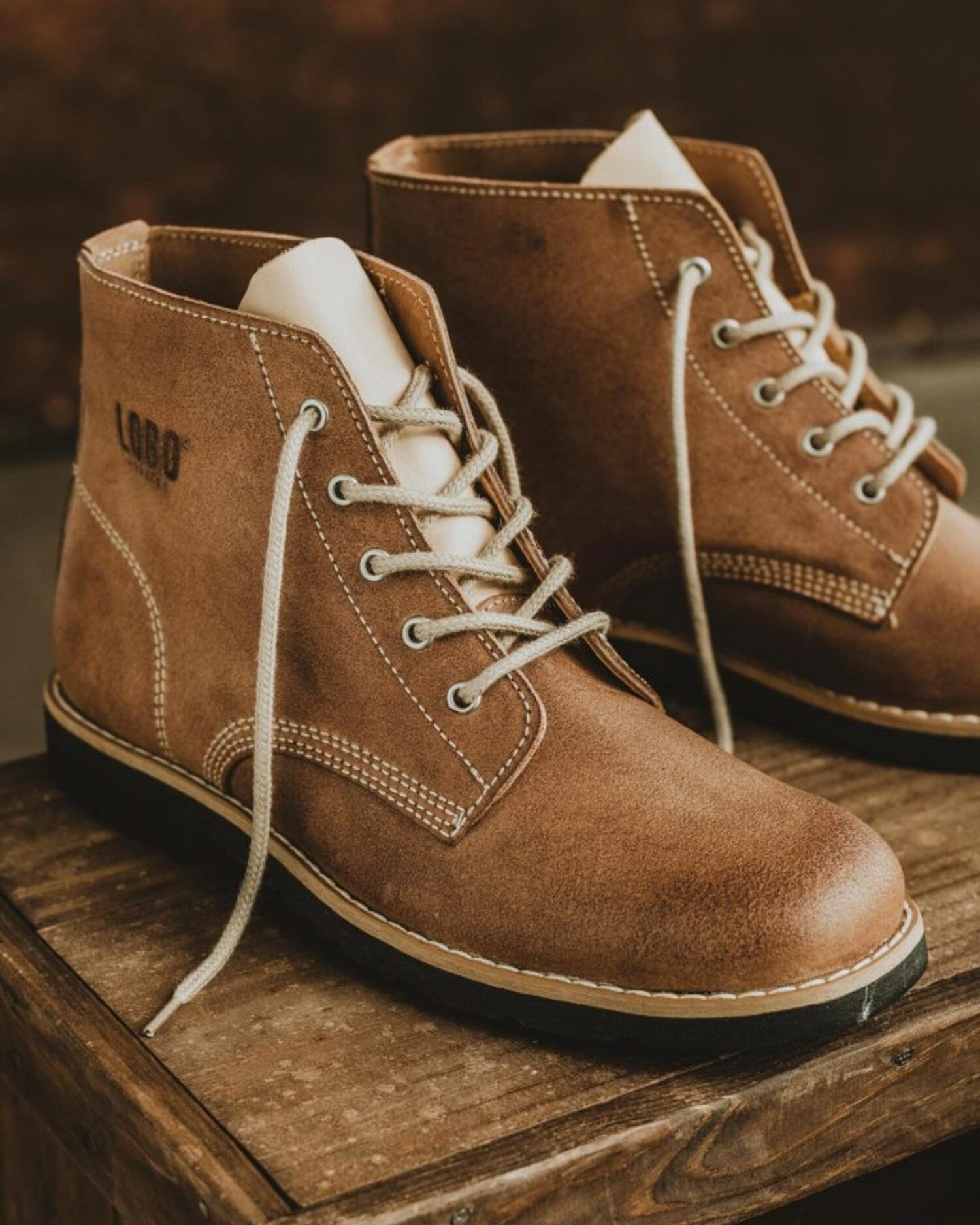 Detail shot of Lobo Raw brown leather boots featuring cream laces on a rustic wooden background.