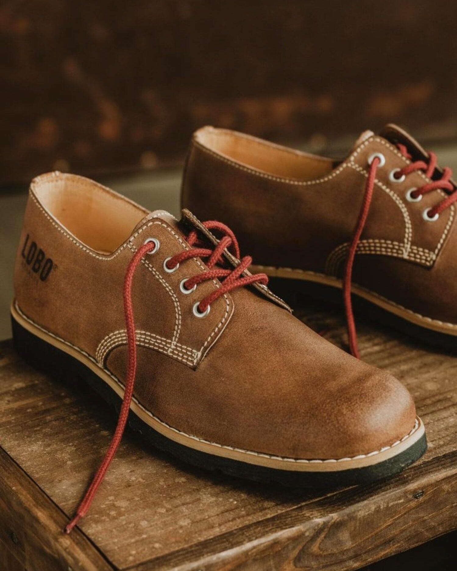 Lobo Raw leather shoes in brown with red laces, Goodyear Welt construction on a rustic wooden surface.