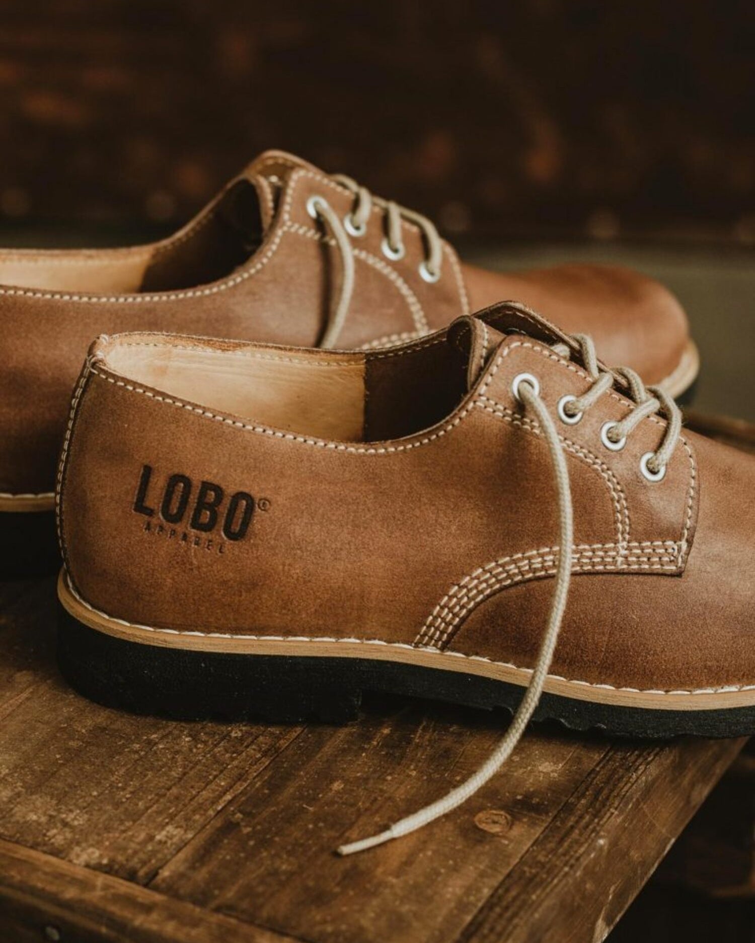 Side view of brown leather shoes with Lobo Apparel logo embossed on the heel and black rubber sole.