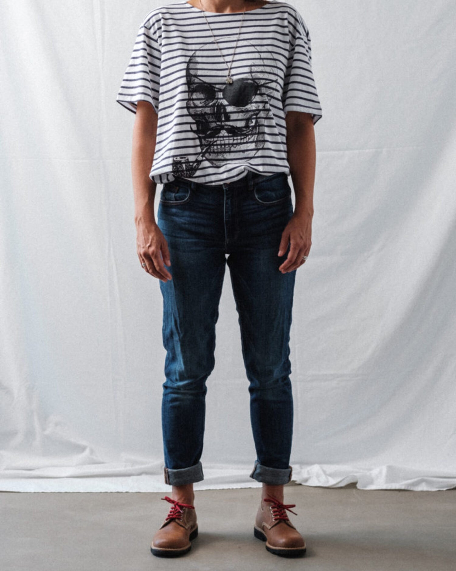 Woman wearing brown Lobo Raw shoes with red laces, styled with dark denim jeans and a striped t-shirt.