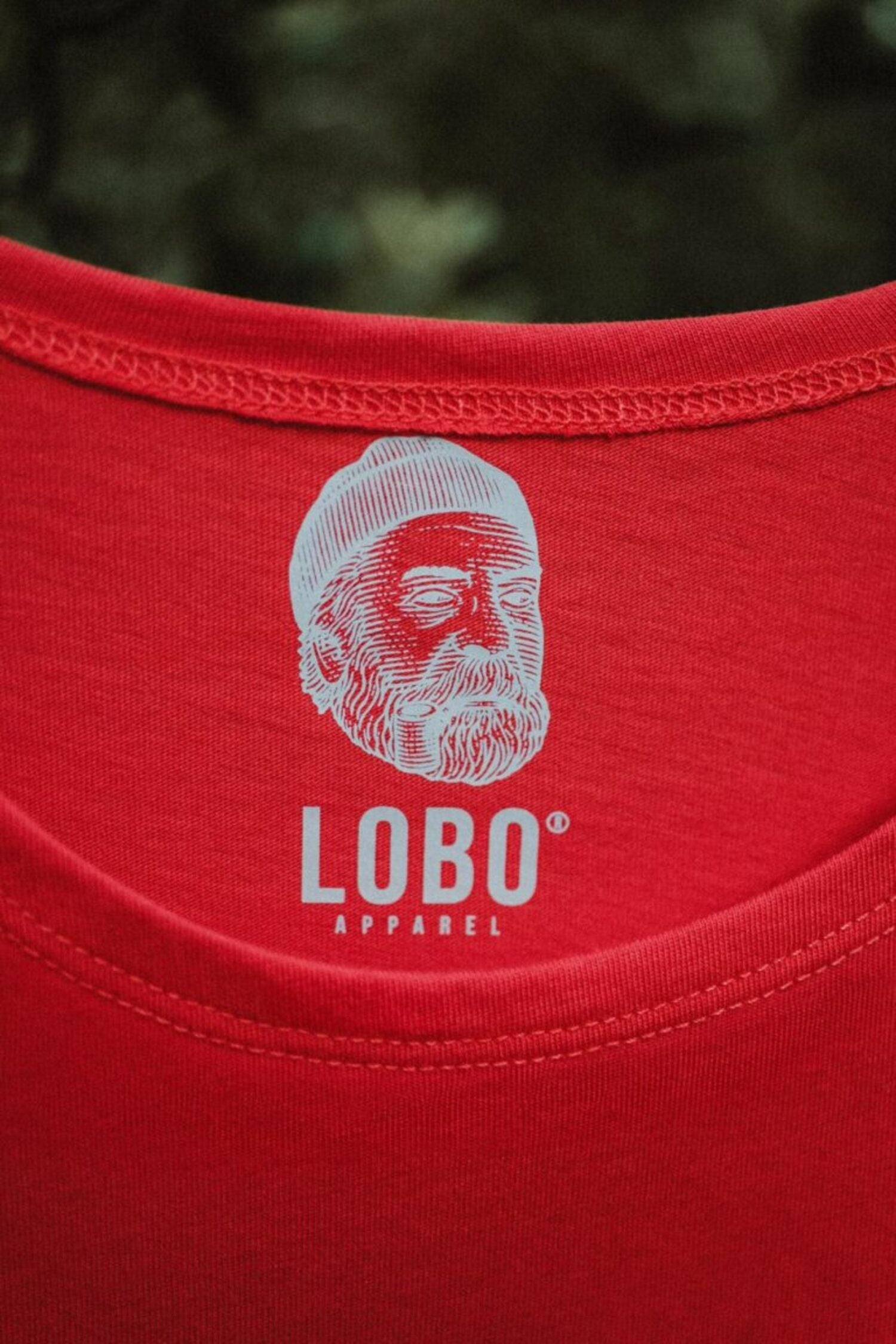 Close-up of the inner neckline of a red LOBO Apparel t-shirt, featuring the white screen-printed logo of a man wearing a beanie and smoking a pipe.