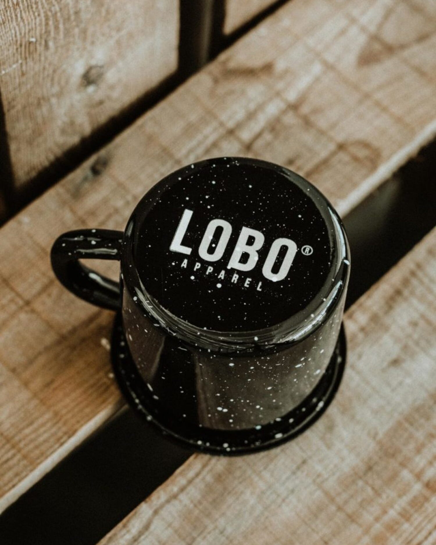 Top view of the inverted black Lobo Skull Enamel mug, revealing the Lobo Apparel logo on the base over a wooden surface.