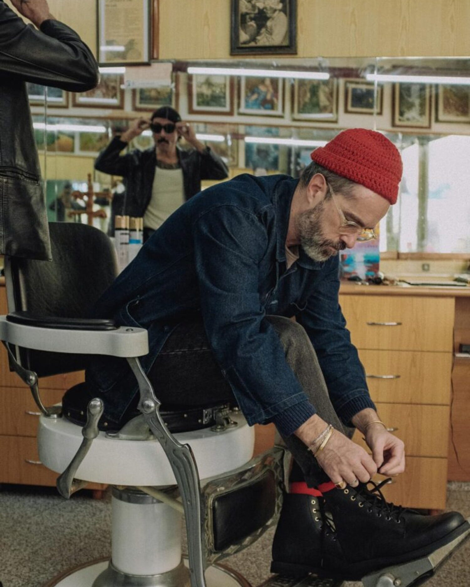 Man sitting in a classic barbershop chair putting on the Lobo Tigre Boots 3rd Edition, demonstrating the fit and rugged style of the footwear.