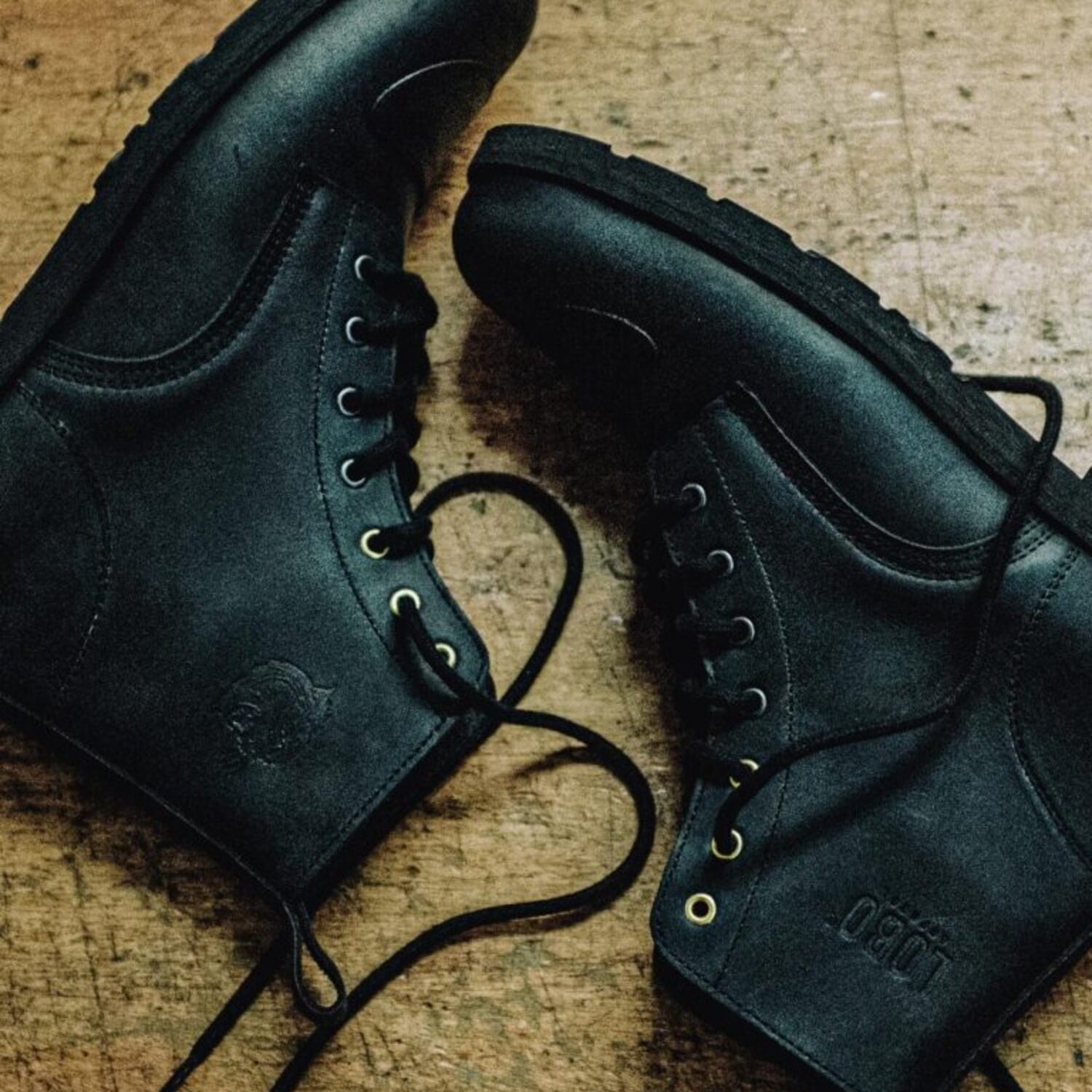 Pair of black leather Lobo Tigre Boots 3rd Edition on wood, showing the motorcycle shifter protection reinforcement and golden eyelets.