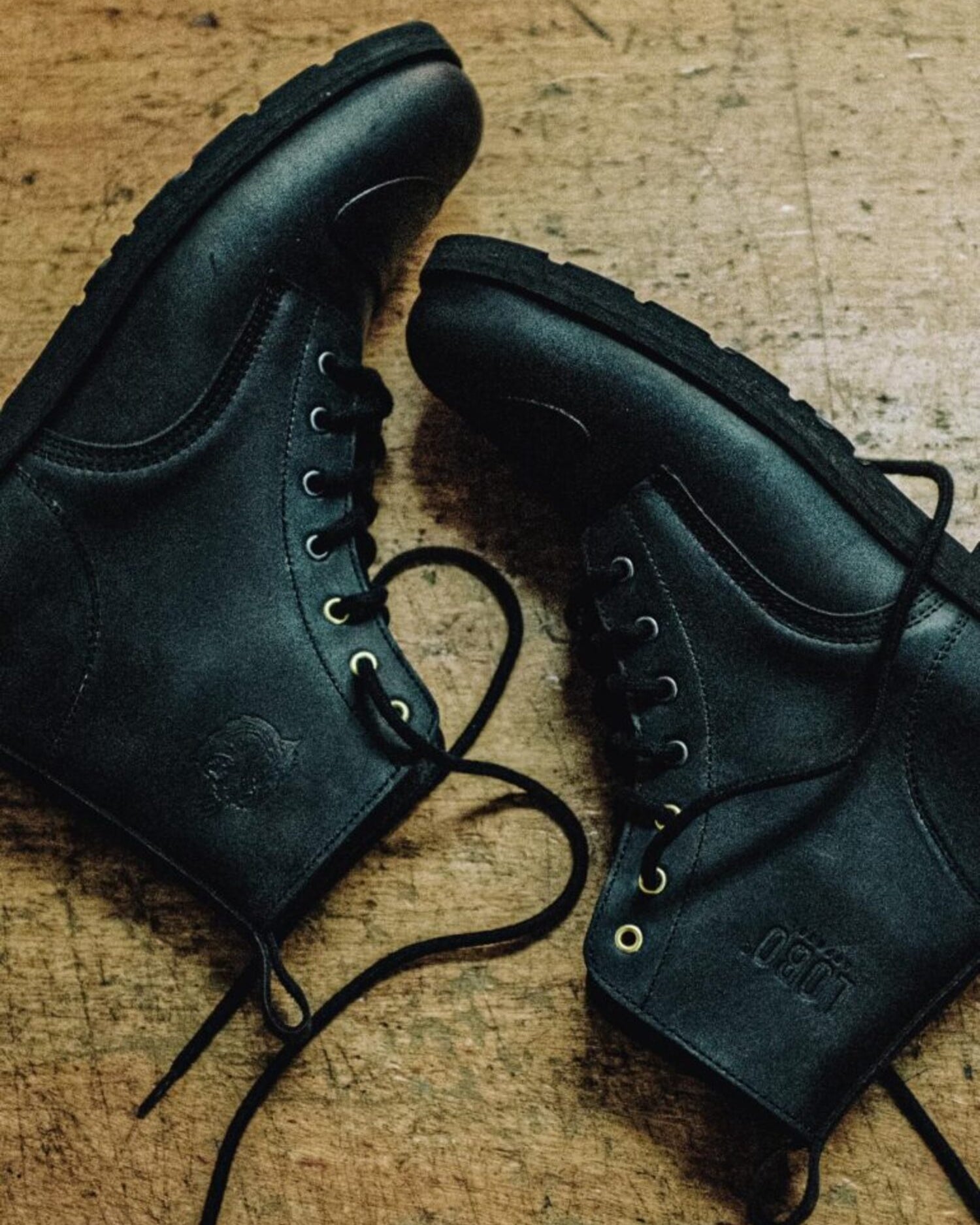Pair of black leather Lobo Tigre Boots 3rd Edition on wood, showing the motorcycle shifter protection reinforcement and golden eyelets.