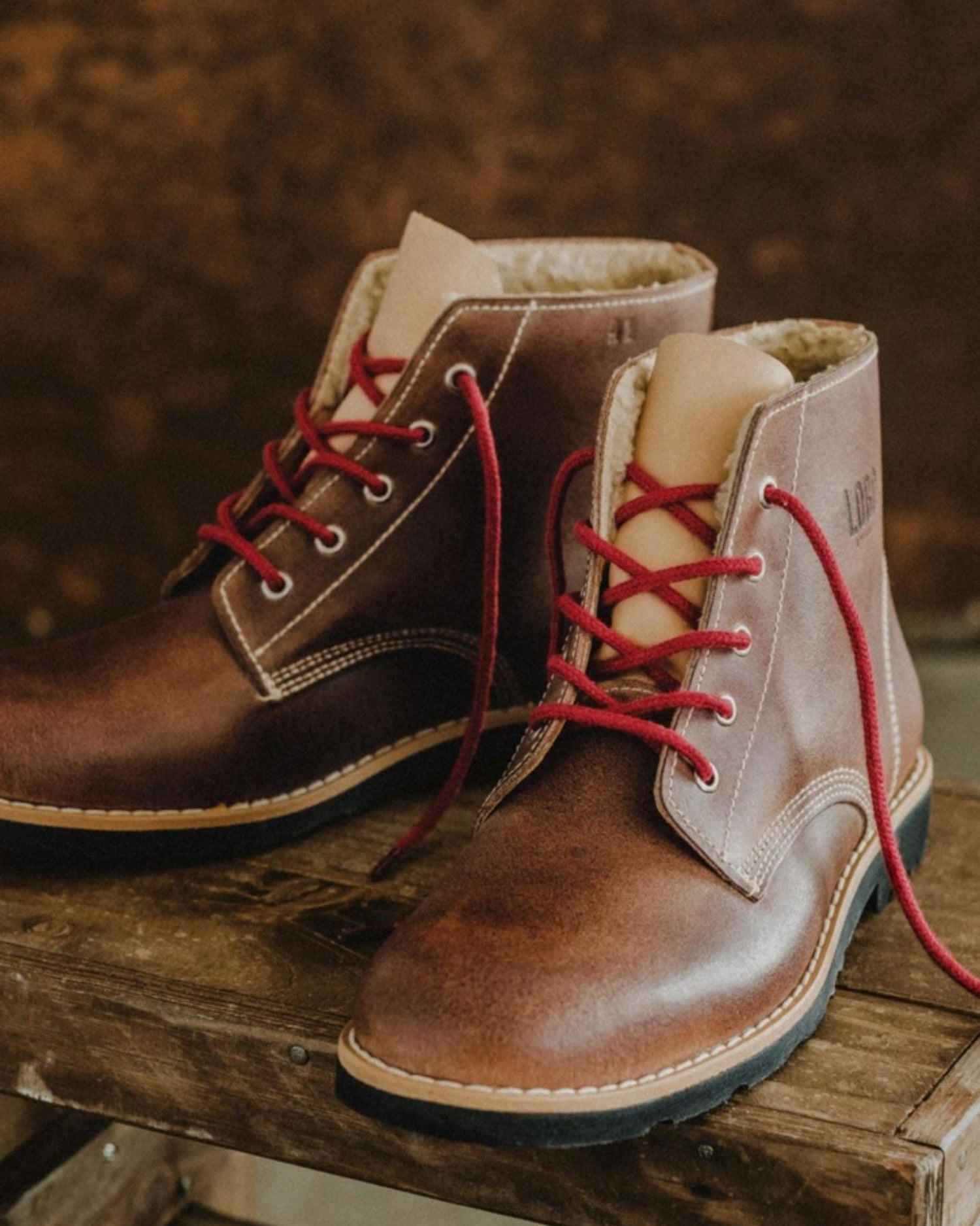 Lobo Warm Boots in brown leather featuring red laces and wool lining on a wooden bench.