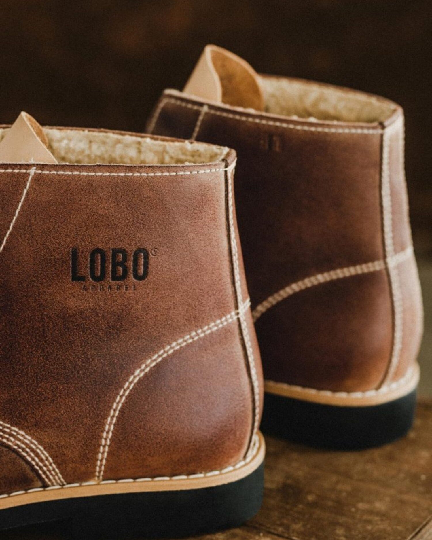 Close-up of the Lobo Apparel logo embossed on the side heel of the brown leather boots.