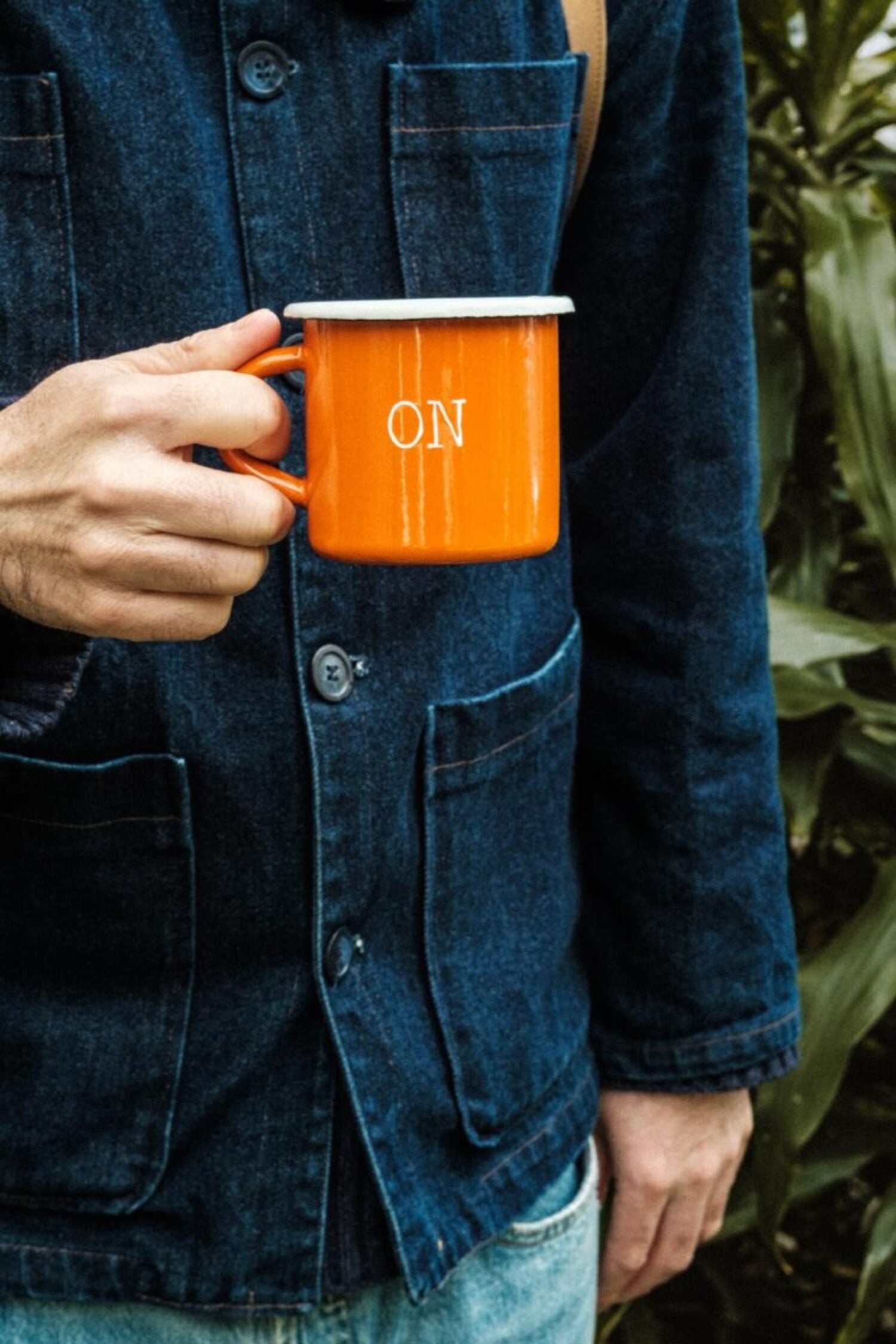Man in a denim chore coat holding the Lobo x Naked Malt orange enamel mug with the ON inscription.