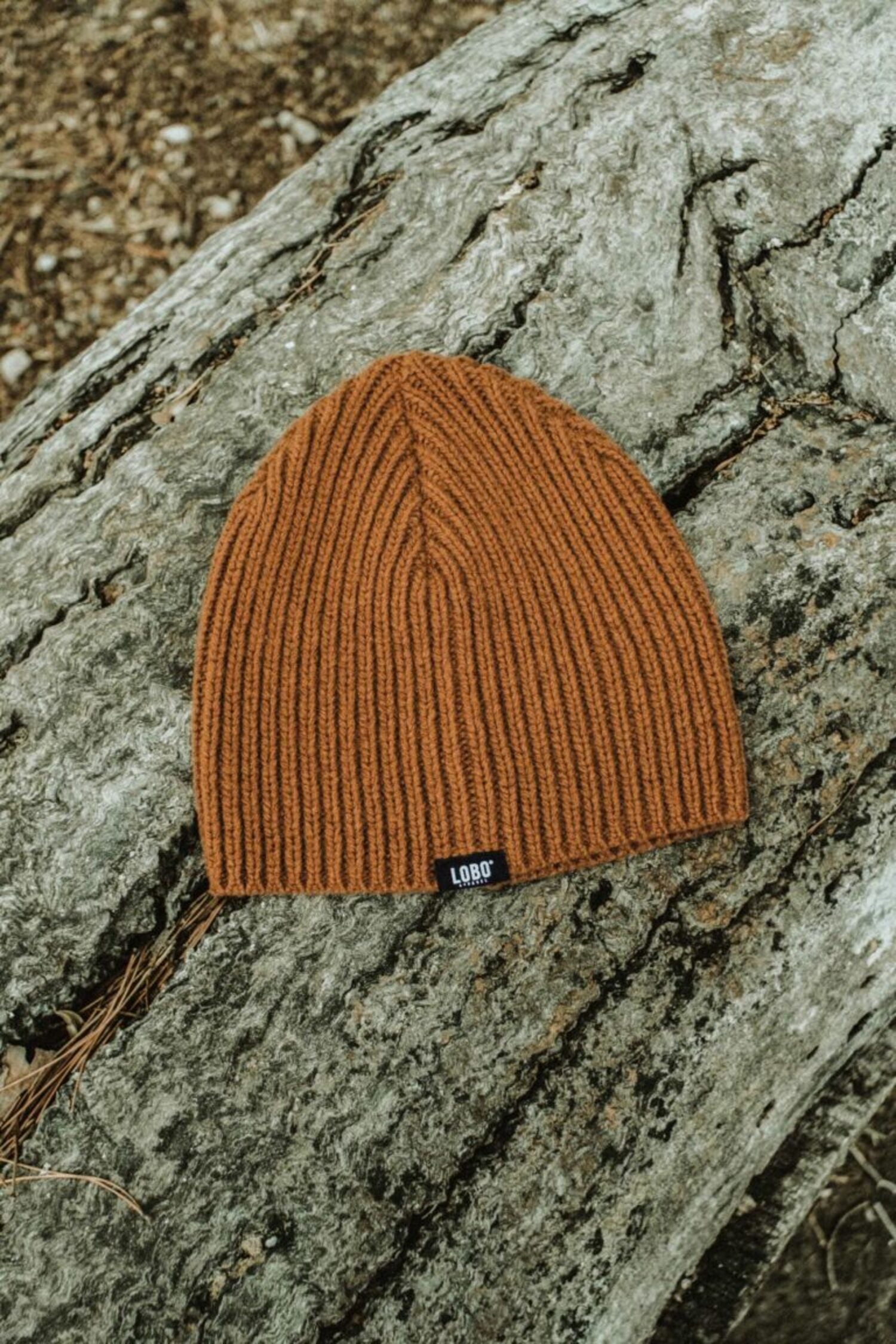 Unisex Manuel Brown Beanie wool hat in rust brown, featuring a ribbed knit and Lobo label, displayed on a tree log.