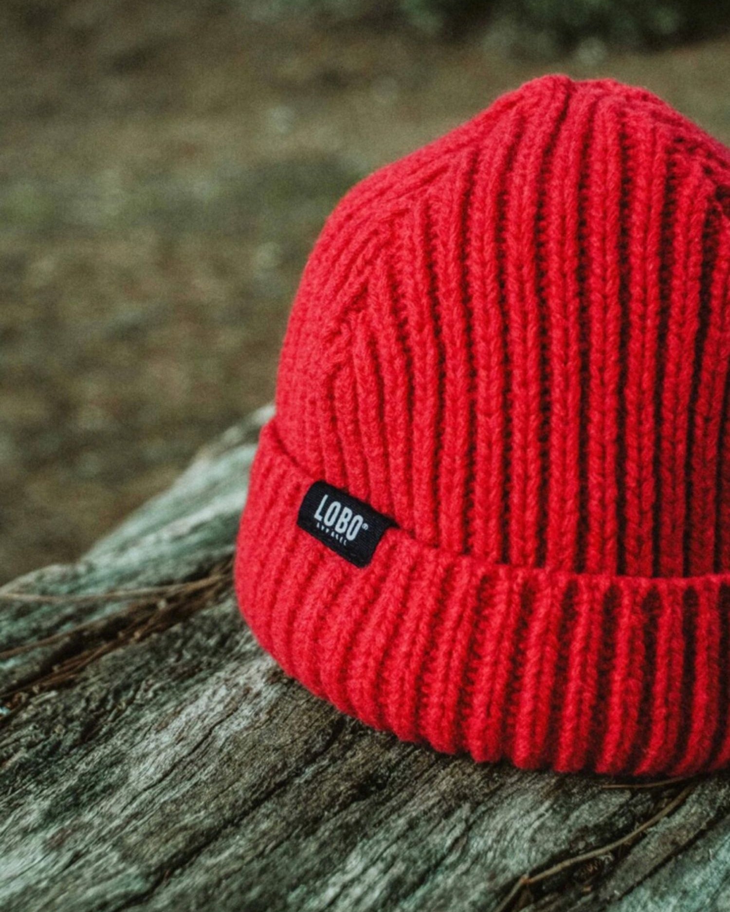 Red wool Manuel Red Beanie from LOBO Apparel resting on a tree log, featuring a visible black logo label.