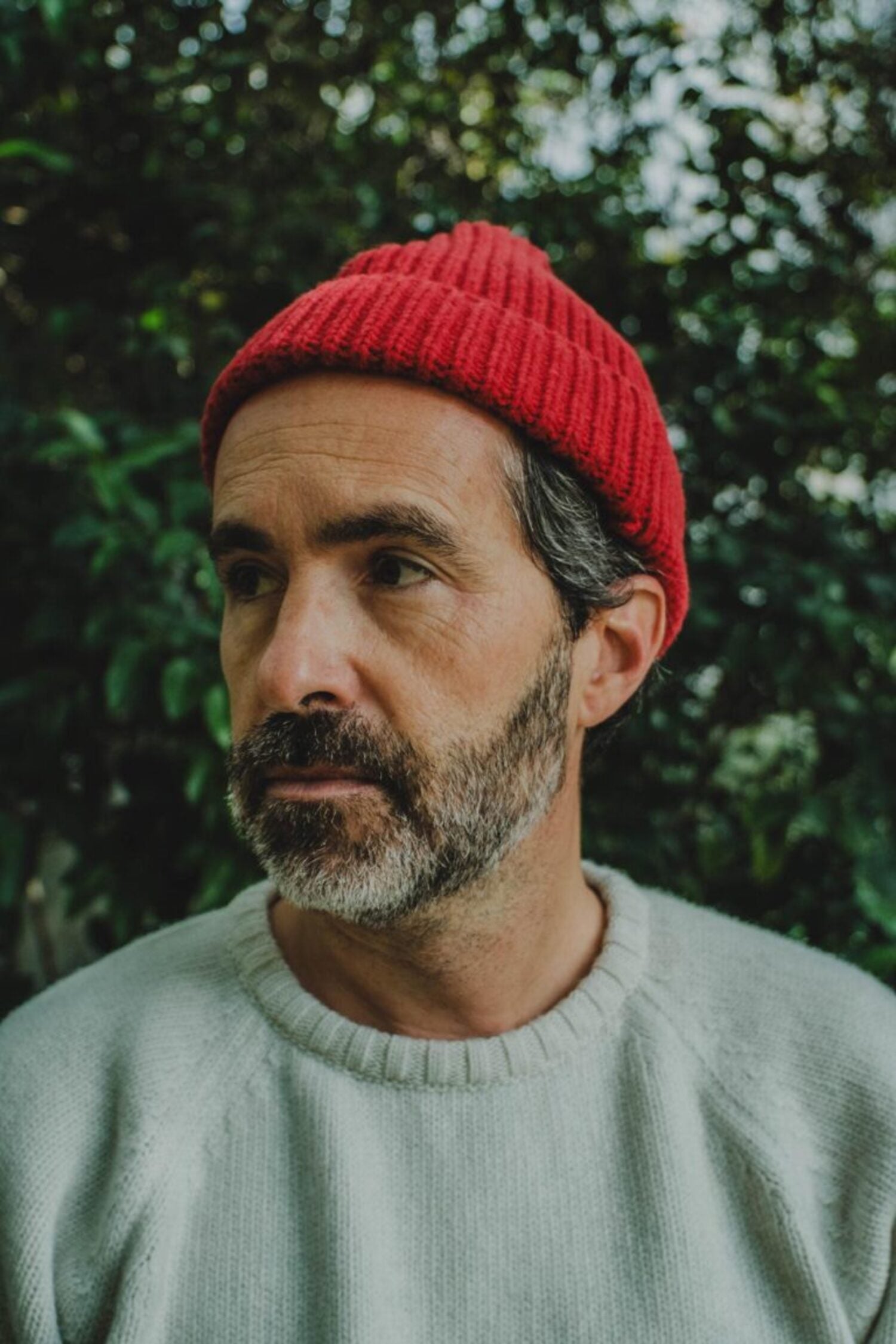 Bearded man wearing the red Manuel Red Beanie wool hat, made in Portugal, in an outdoor setting.