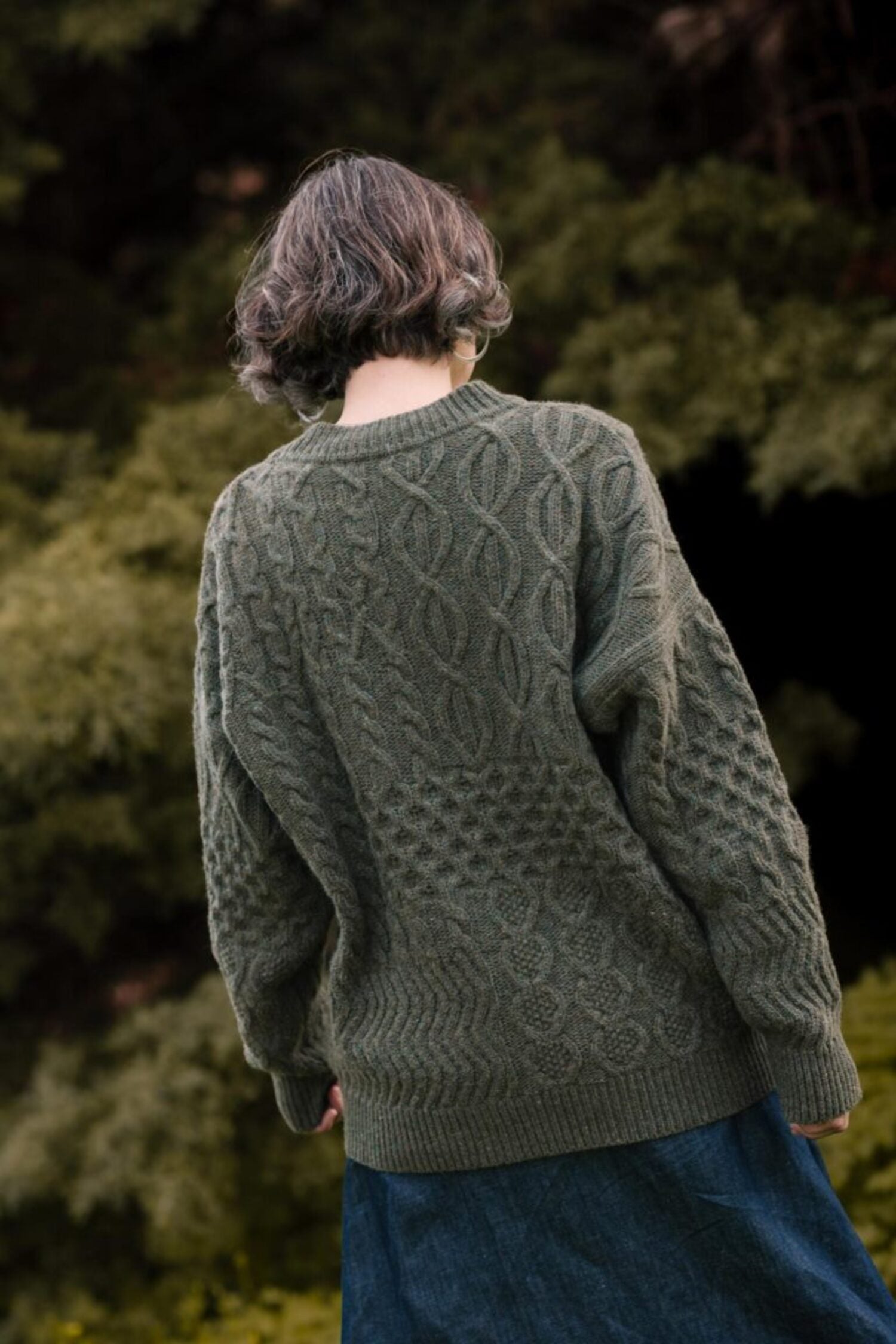Back view of the Lobo Apparel unisex Verde Grisalho sweater, showcasing the textured knit pattern and comfortable fit in a natural outdoor setting.