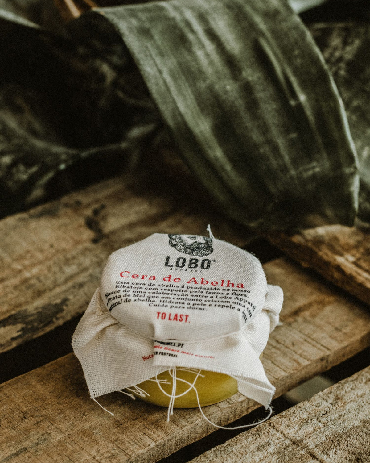Lobo natural beeswax leather conditioner jar with rustic fabric cover, set on wood in an organic setting.