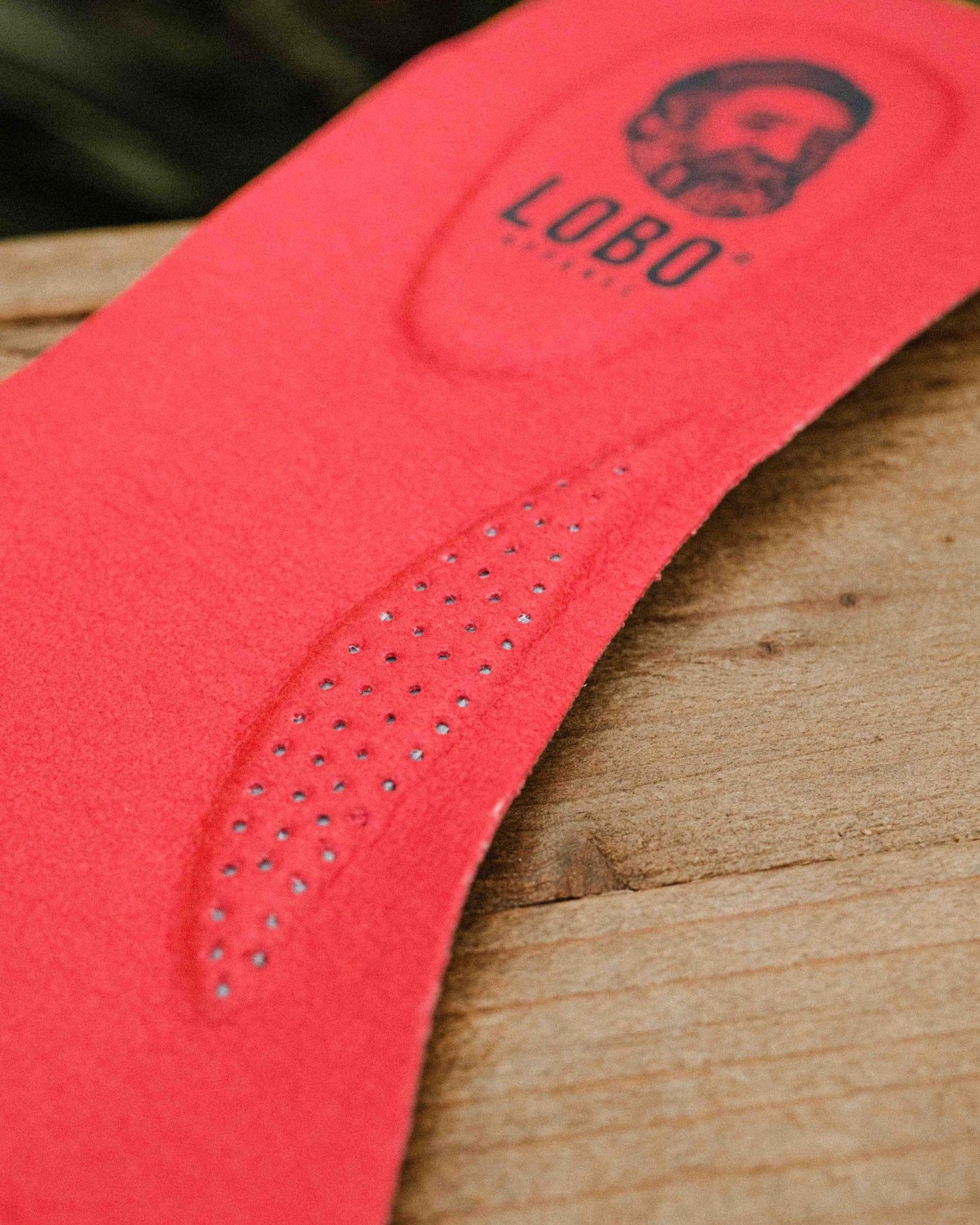 Top view of two red Lobo Insoles leather insoles with visible logo on a wooden box.