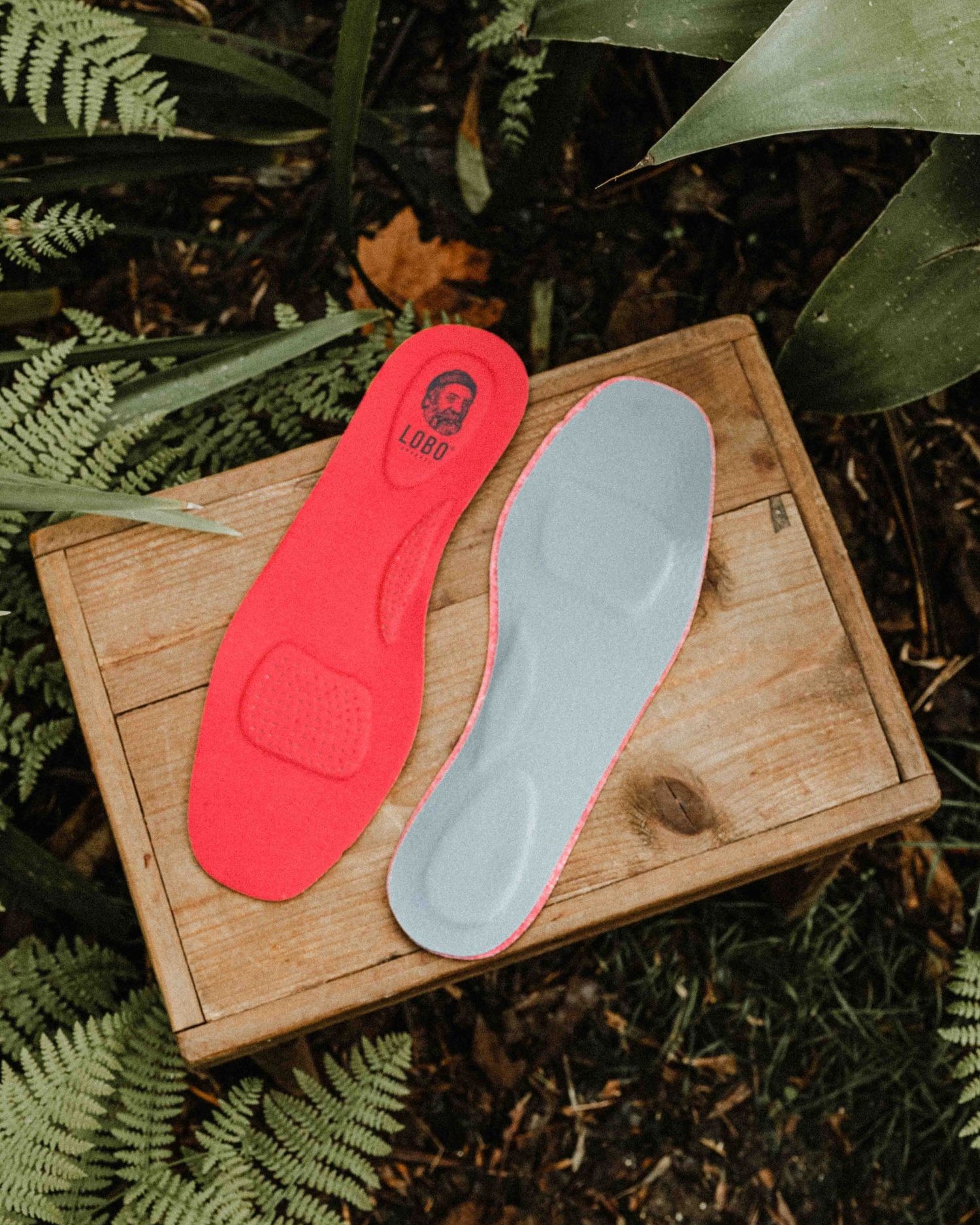 Pair of red Lobo Insoles leather insoles photographed from above on a wooden box in a natural setting.
