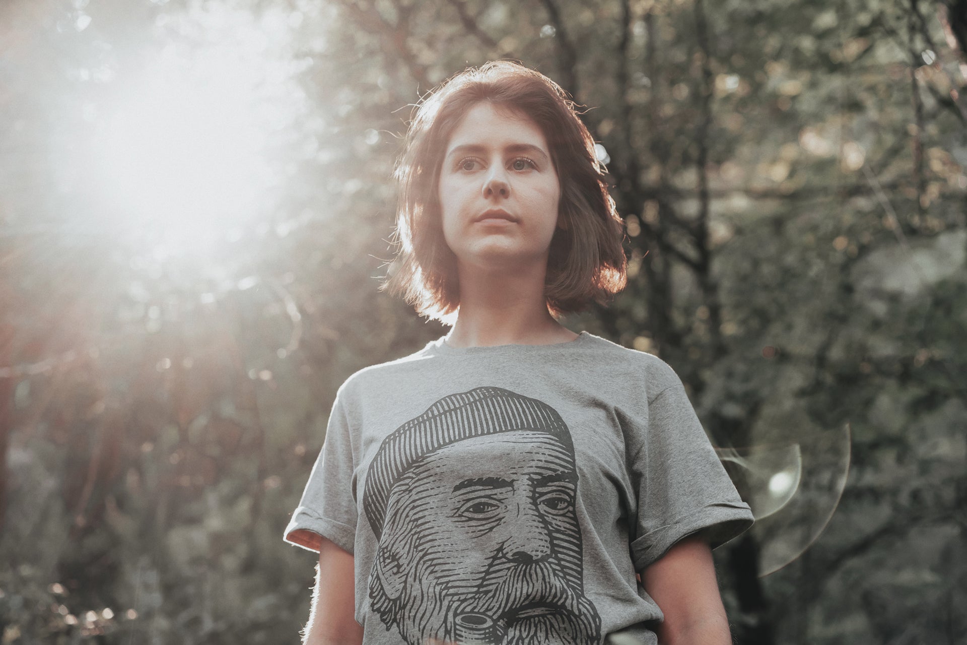 Lifestyle portrait of a woman in nature, wearing the essential LOBO t-shirt featuring the logo illustration: a bearded man with a beanie and pipe.