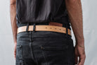 Back view of a man wearing a tan leather belt with black jeans, emphasizing the clean and functional design.