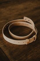 Tan genuine leather belt by Lobo Apparel, coiled, showing internal "LOBO APPAREL TO LAST" embossing on a wooden background.