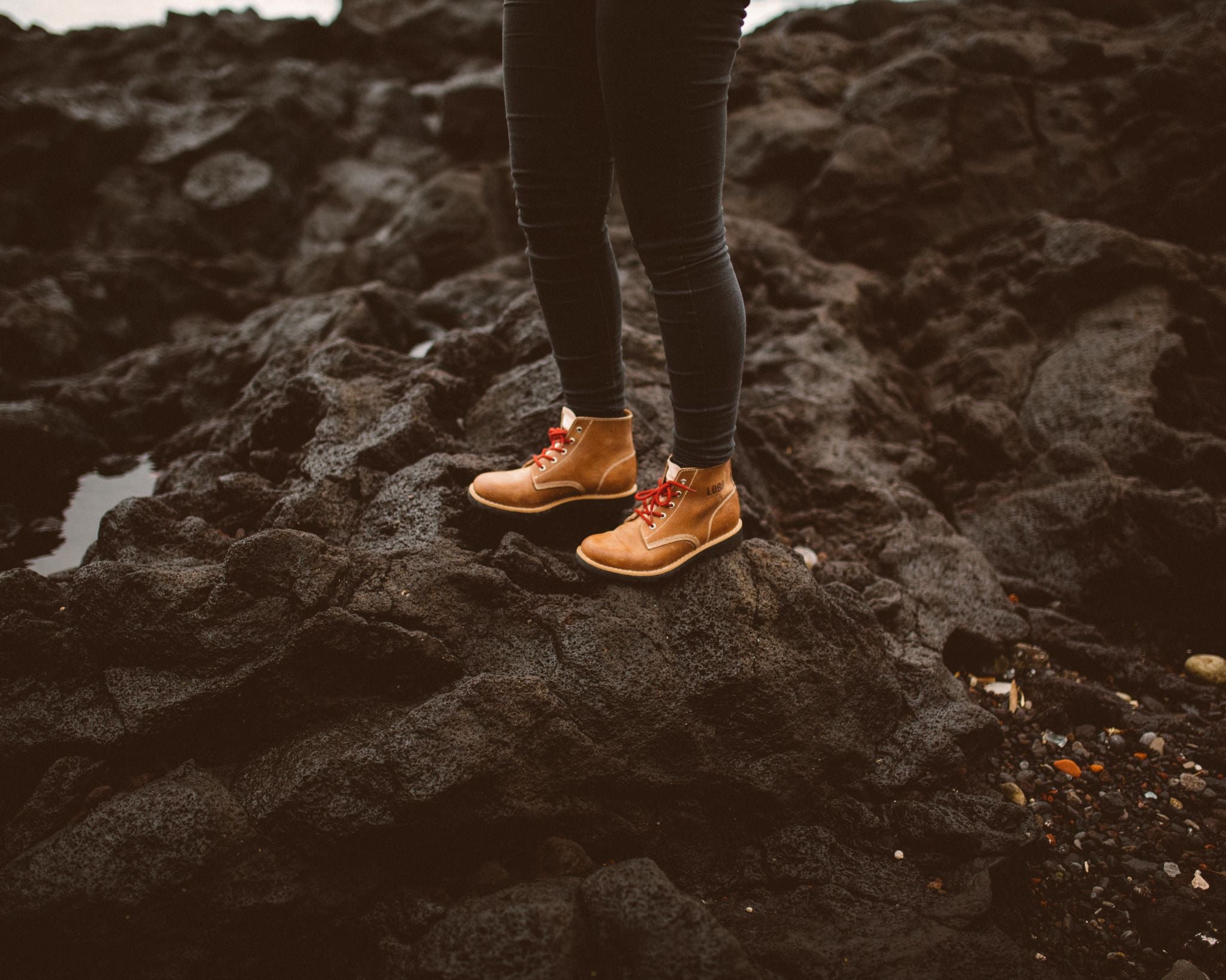 RAW brown leather boots with red laces on volcanic rocks in São Miguel Island, Azores.