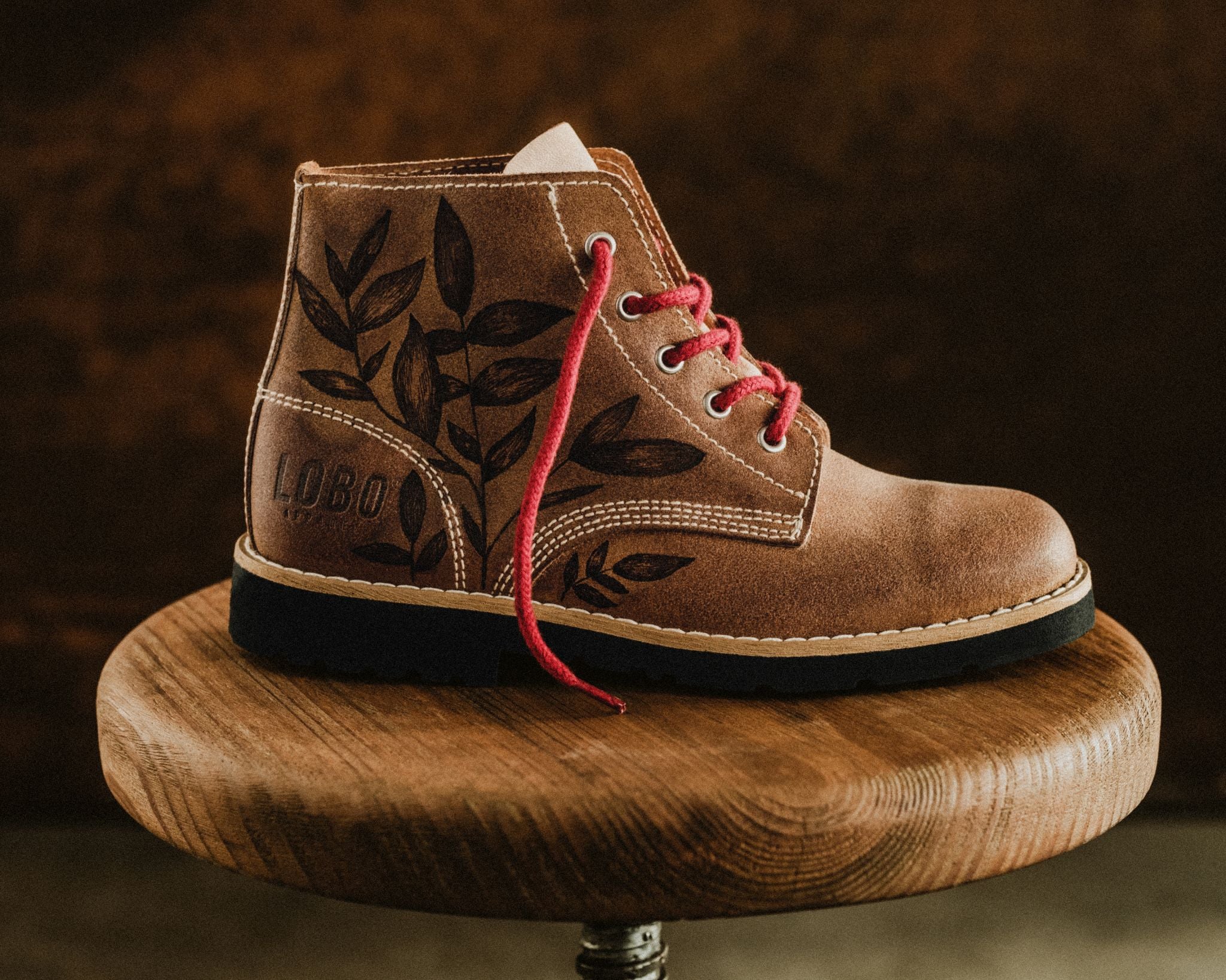 Side profile view of the Lobo Raw Boots by Cláudia Salgueiro, showcasing the detailed botanical illustration on brown leather, the embossed LOBO logo, and red laces.