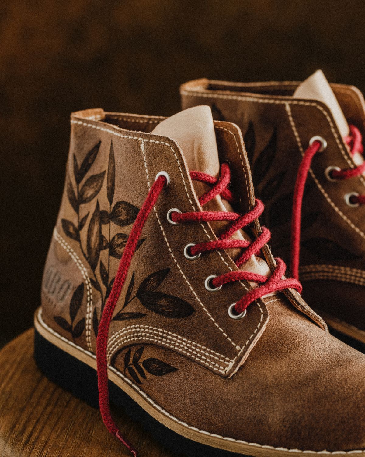 Close-up of the Lobo Raw Boots by Cláudia Salgueiro in genuine leather, showcasing the intertwined red laces and the precision of the hand-drawn leaf illustration.