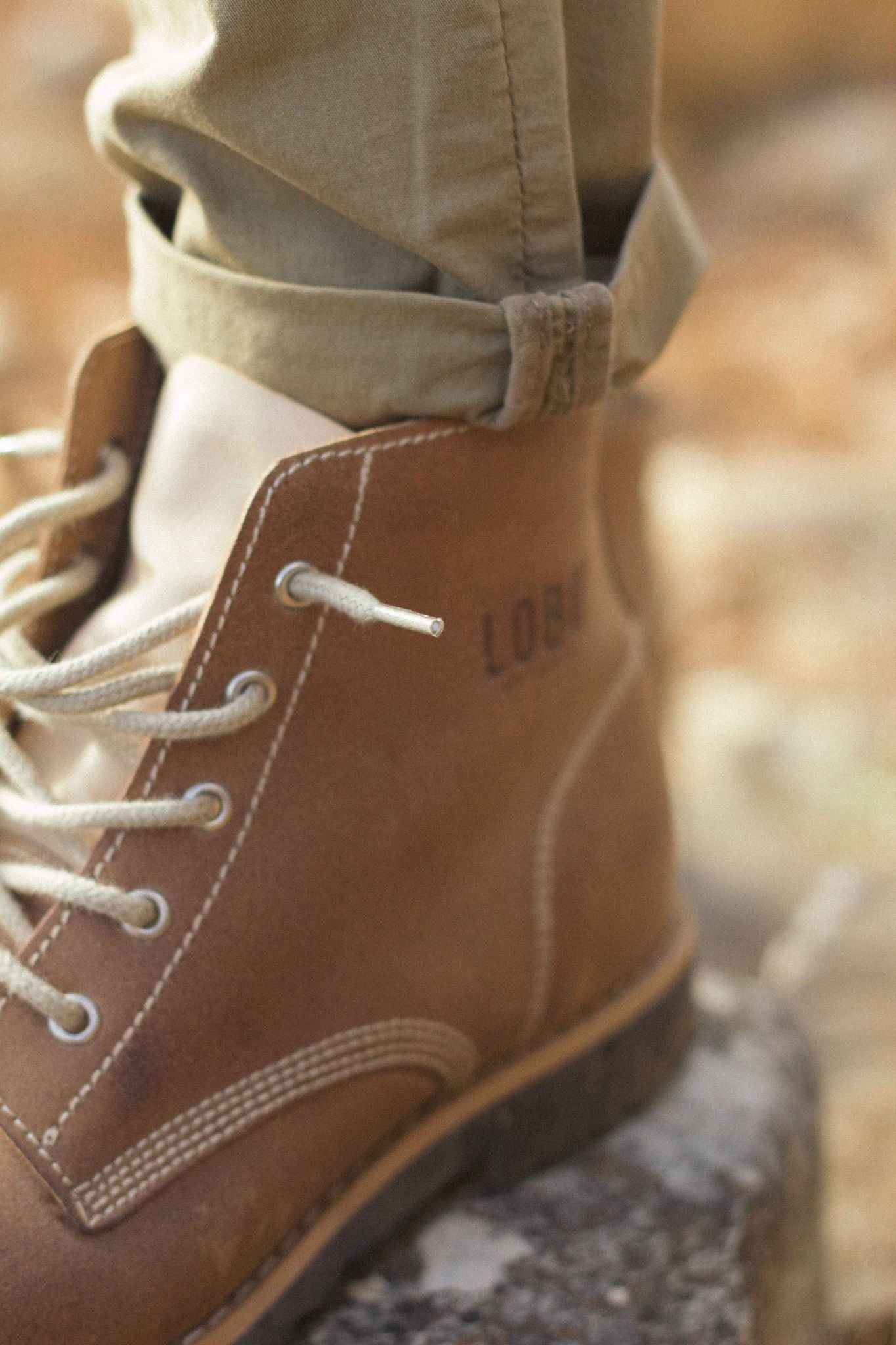 Close-up detail of Lobo Raw Boots in brown leather, showing the embossed logo and light beige rope laces.