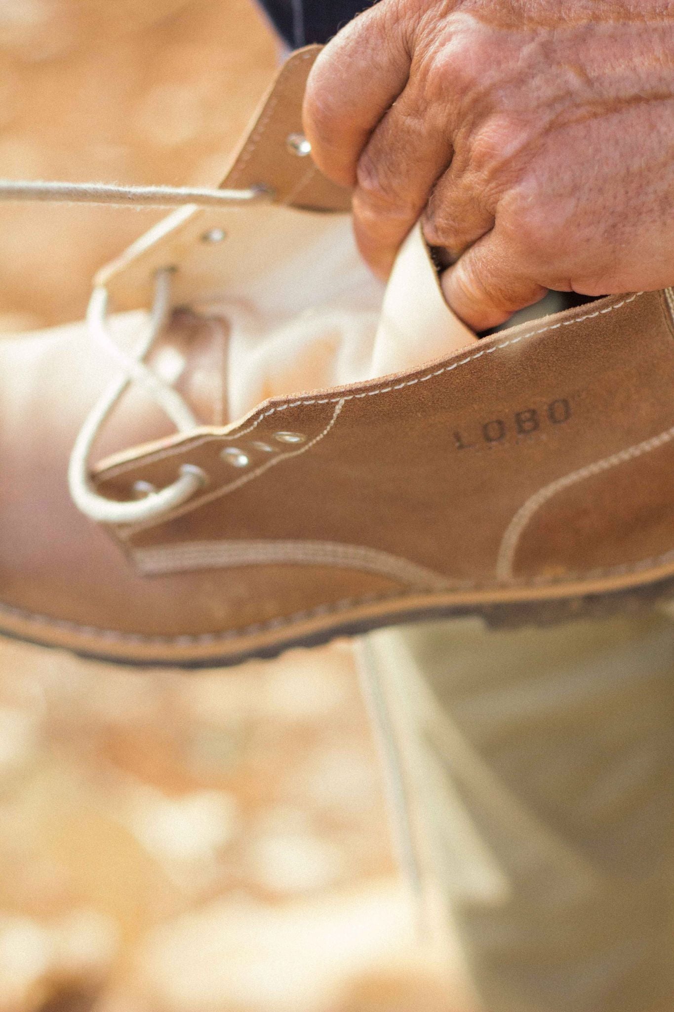 Close-up of a natural leather Lobo Raw Boot, displaying the material's texture, rope laces, and the embossed logo.