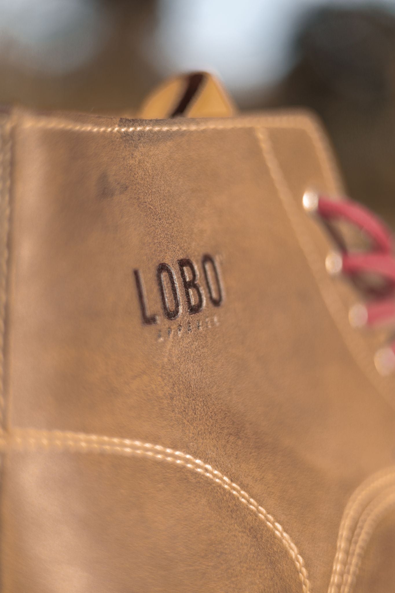 Macro close-up of the "LOBO" logo embossed on the side of the boot, highlighting the natural leather texture and the precision of the light-colored contrast stitching.
