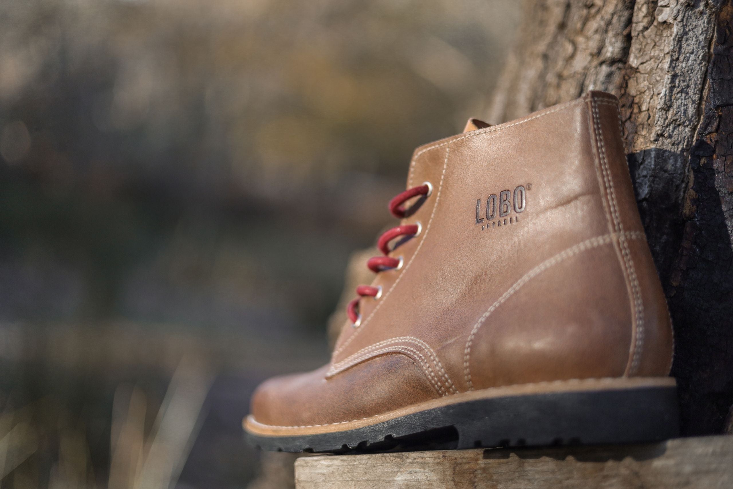 Side medium shot of the Lobo Raw Boots in brown leather, highlighting the heat-embossed Lobo logo, reinforced white stitching, and red laces.