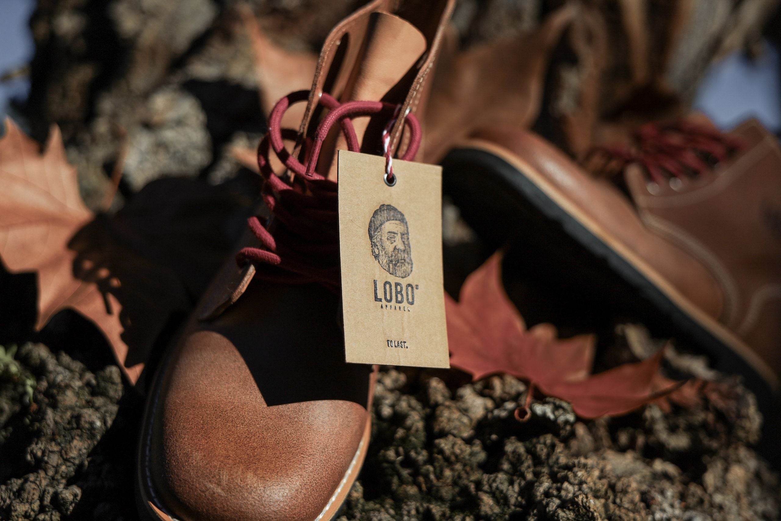 Close-up shot of the Lobo Raw Boots in brown leather, focusing on the handcrafted cardboard tag and the natural leather texture under sunlight.
