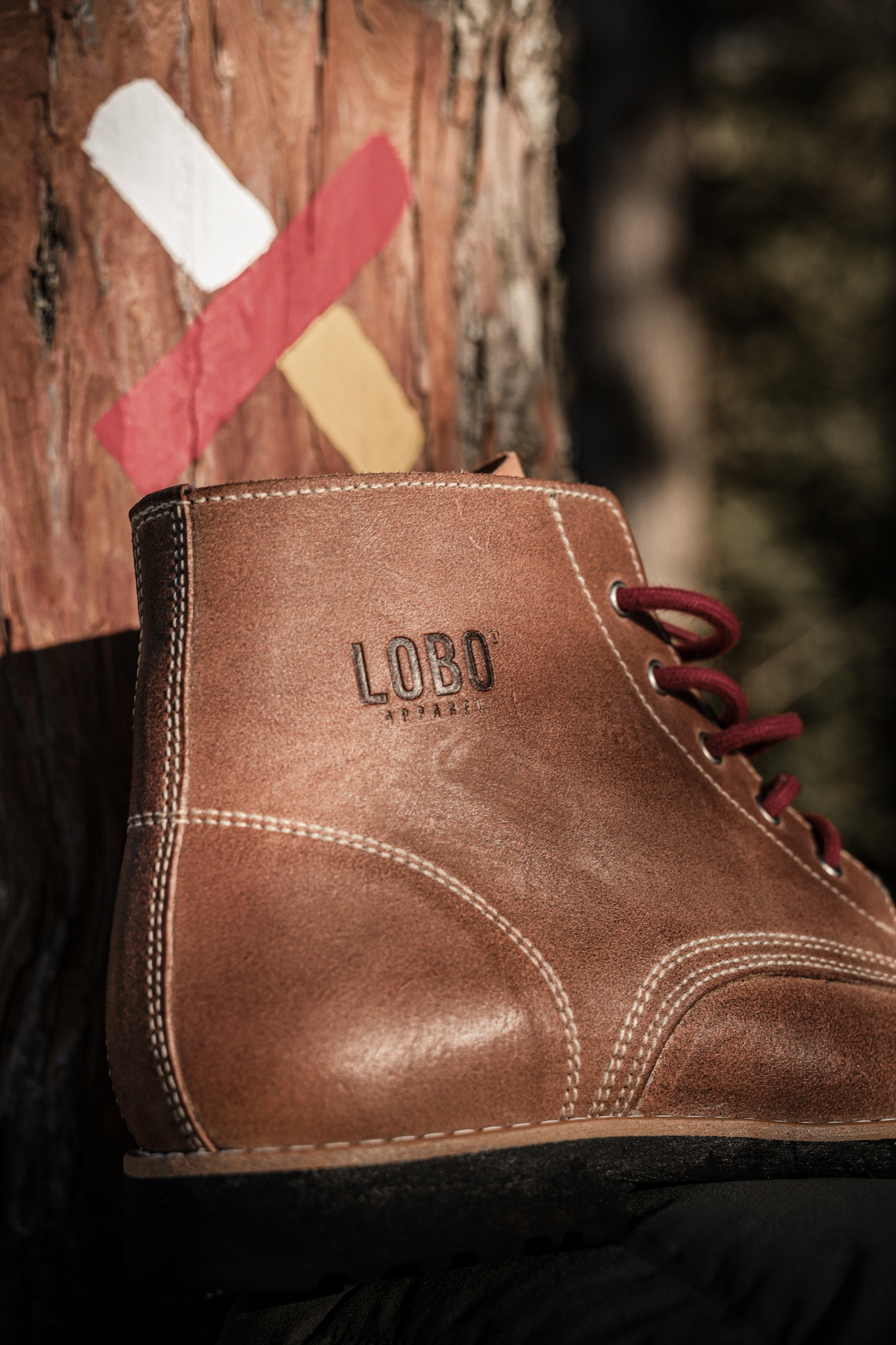 Detailed shot of the side of Lobo Raw Boots, showing the embossed "Lobo" logo on the leather, reinforced stitching, and burgundy laces.