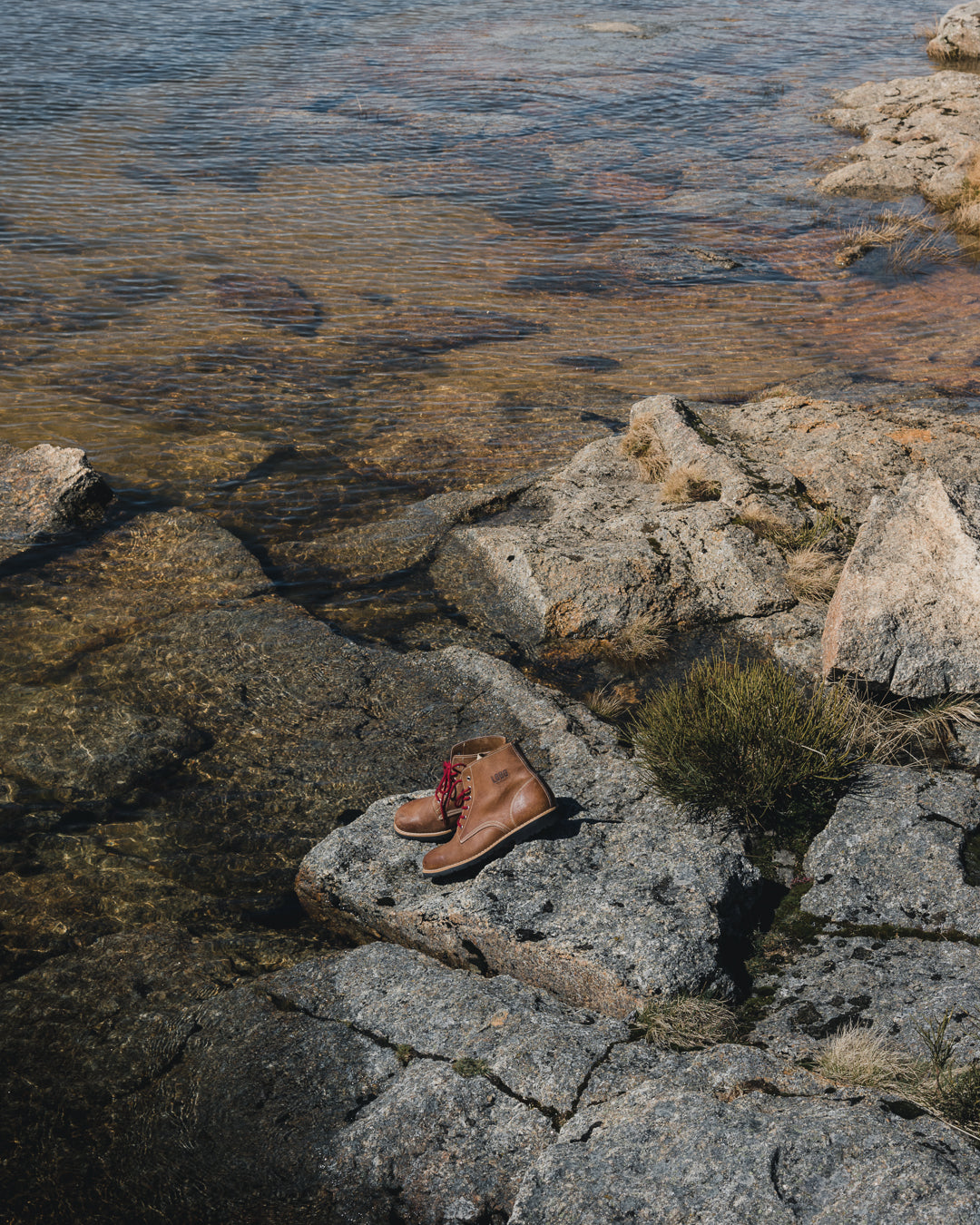 Lobo Raw boots placed on natural rocks by a river, demonstrating the leather's resistance and the ideal sole for uneven and outdoor terrain.