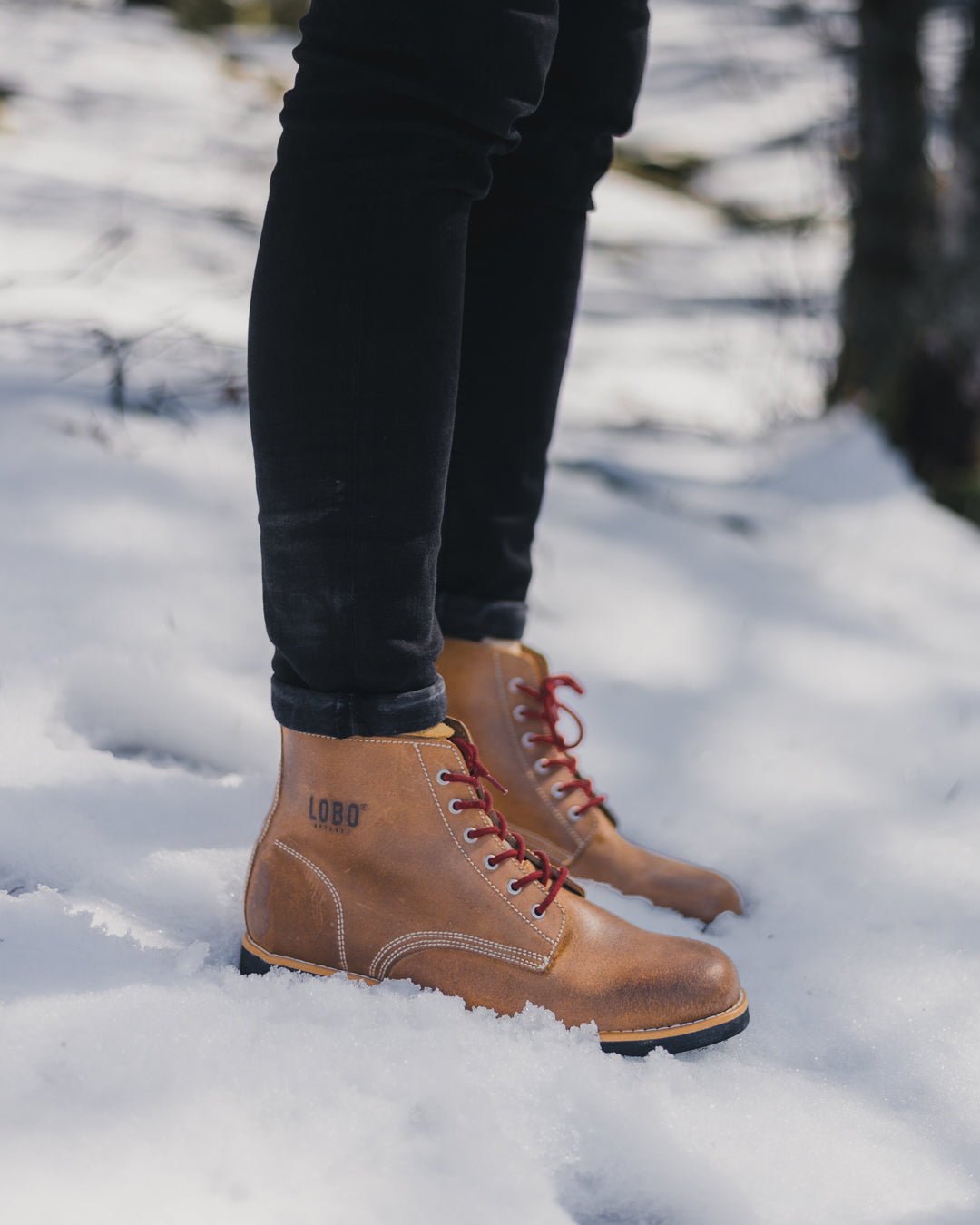 Lobo Raw Boots in brown leather with red laces on white snow, highlighting durability and rugged winter design.