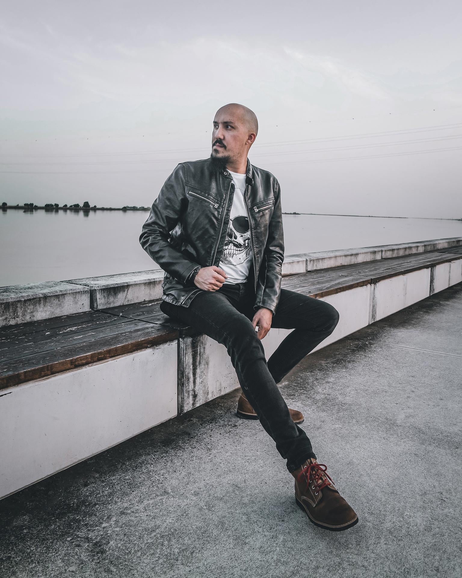 Man in a biker outfit sitting by the river, wearing a black leather jacket and brown Lobo RAW leather boots.