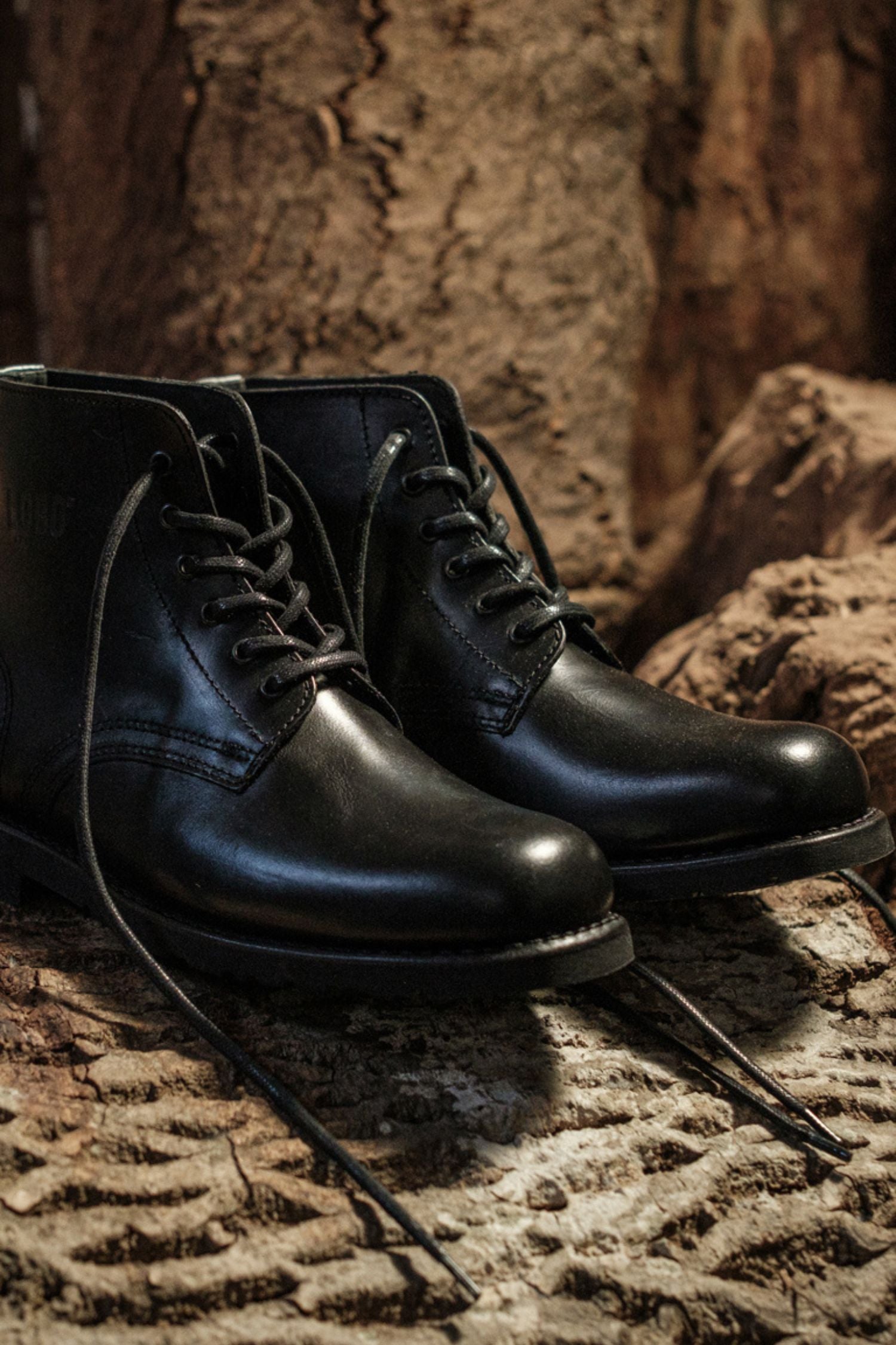 Pair of Lobo All Black leather boots with black cotton laces, Goodyear Welt construction, on a rustic background.