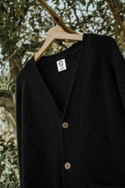 Upper view of the black Lobo Black Wool Cardigan on a hanger, with V-neck, Lobo label and front buttons.