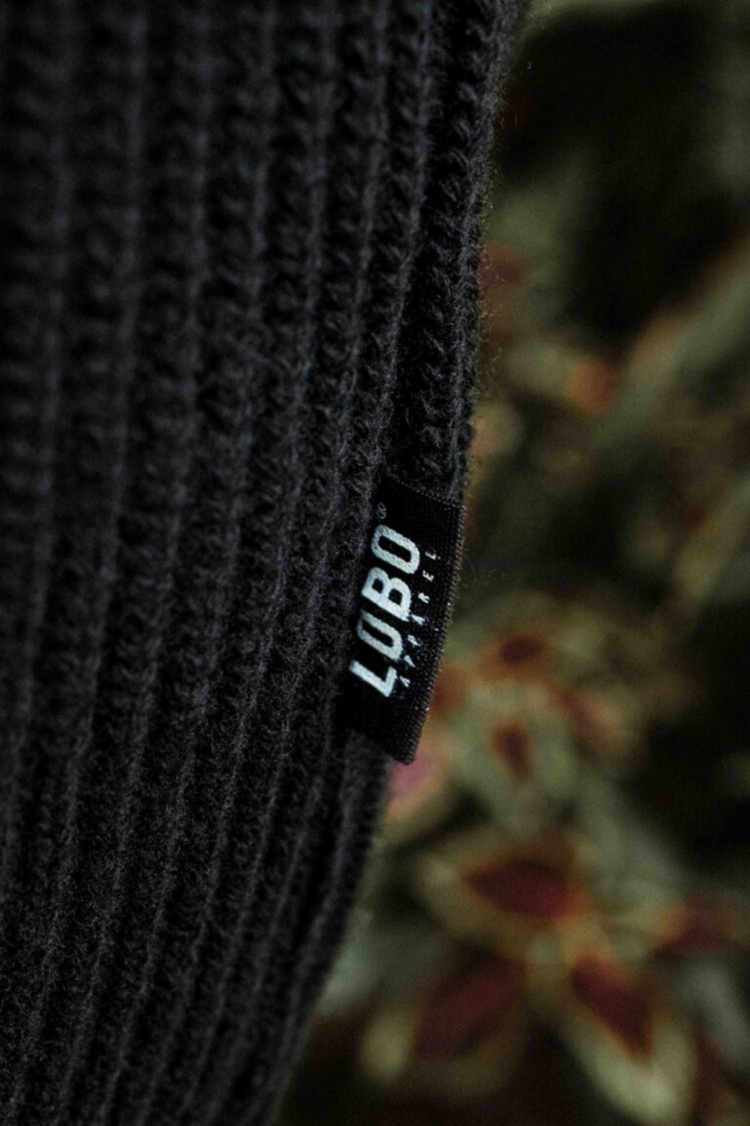 Close-up of the black knit fabric of the Lobo Black Wool Cardigan with the Lobo Apparel side label.