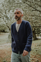 Man wearing the Lobo Apparel denim blue wool cardigan with a grey t-shirt, walking in an outdoor garden setting.